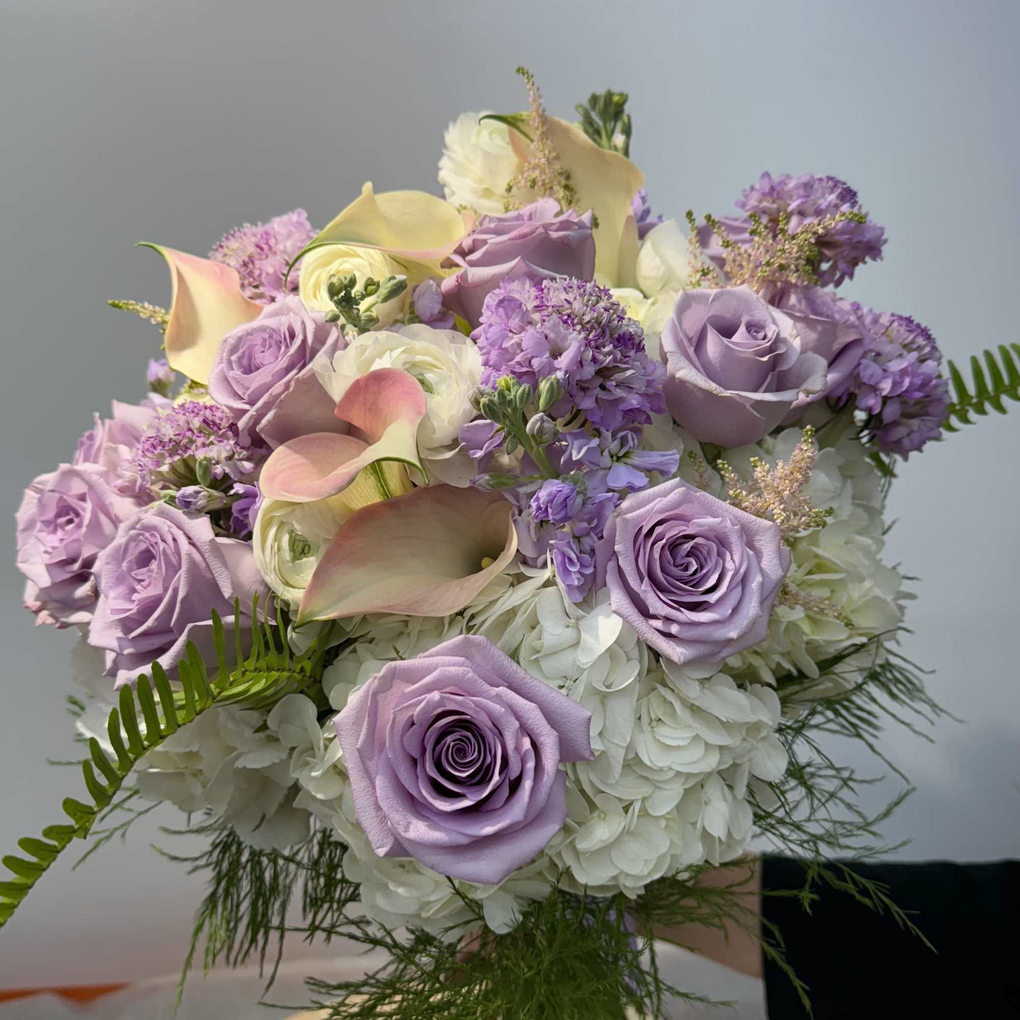 Lavender roses and calla lilies arranged with white hydrangeas.