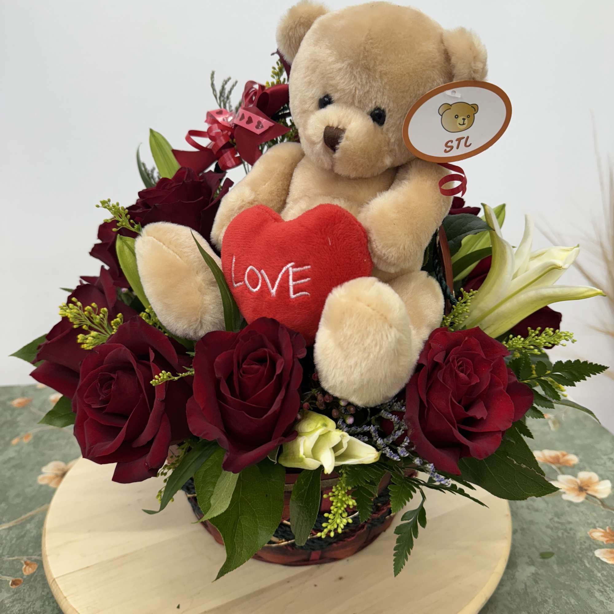 Teddy bear with a red heart surrounded by red roses in a basket