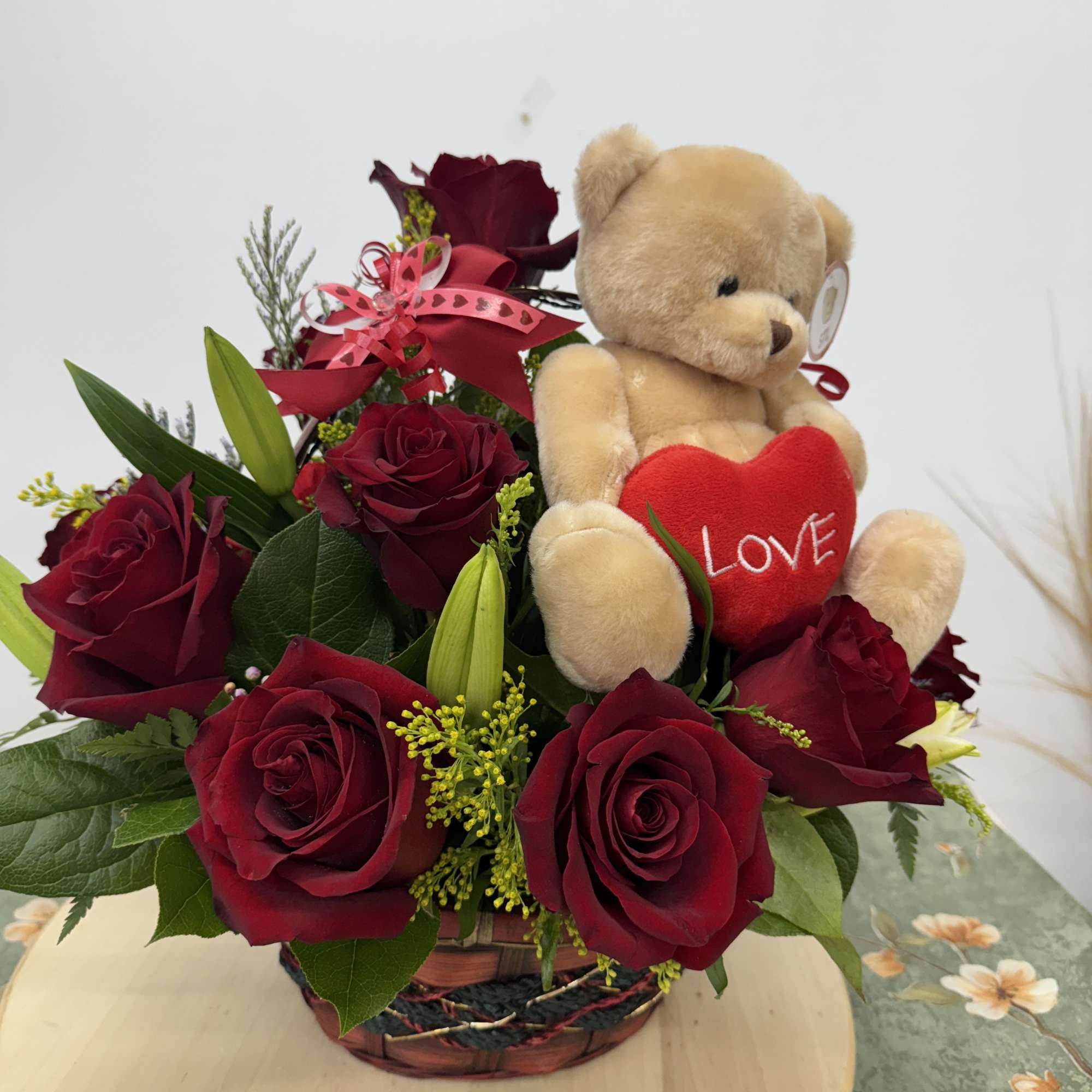 Red rose arrangement with a teddy bear holding a heart in a basket