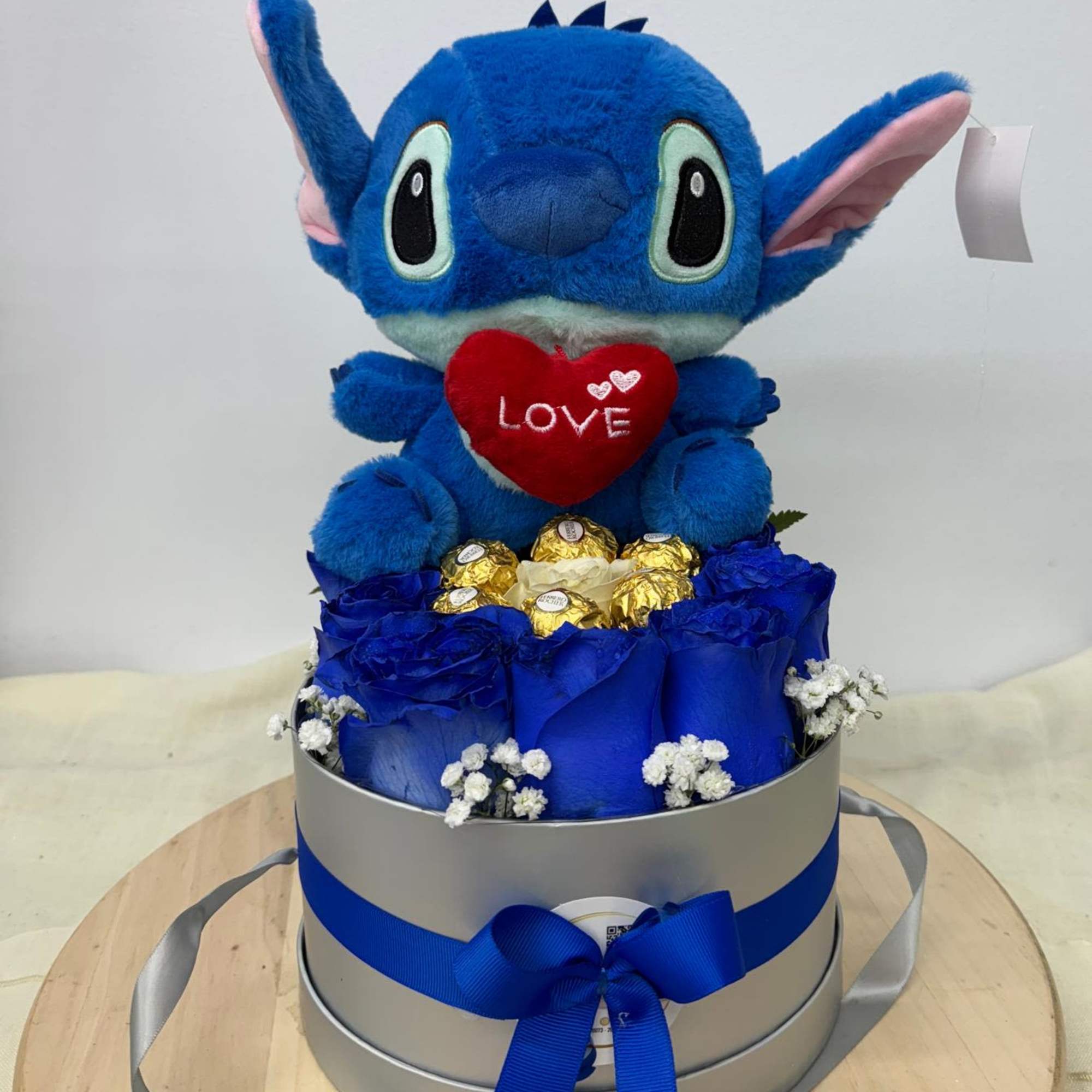 Blue plush character in a gift box with roses and chocolates