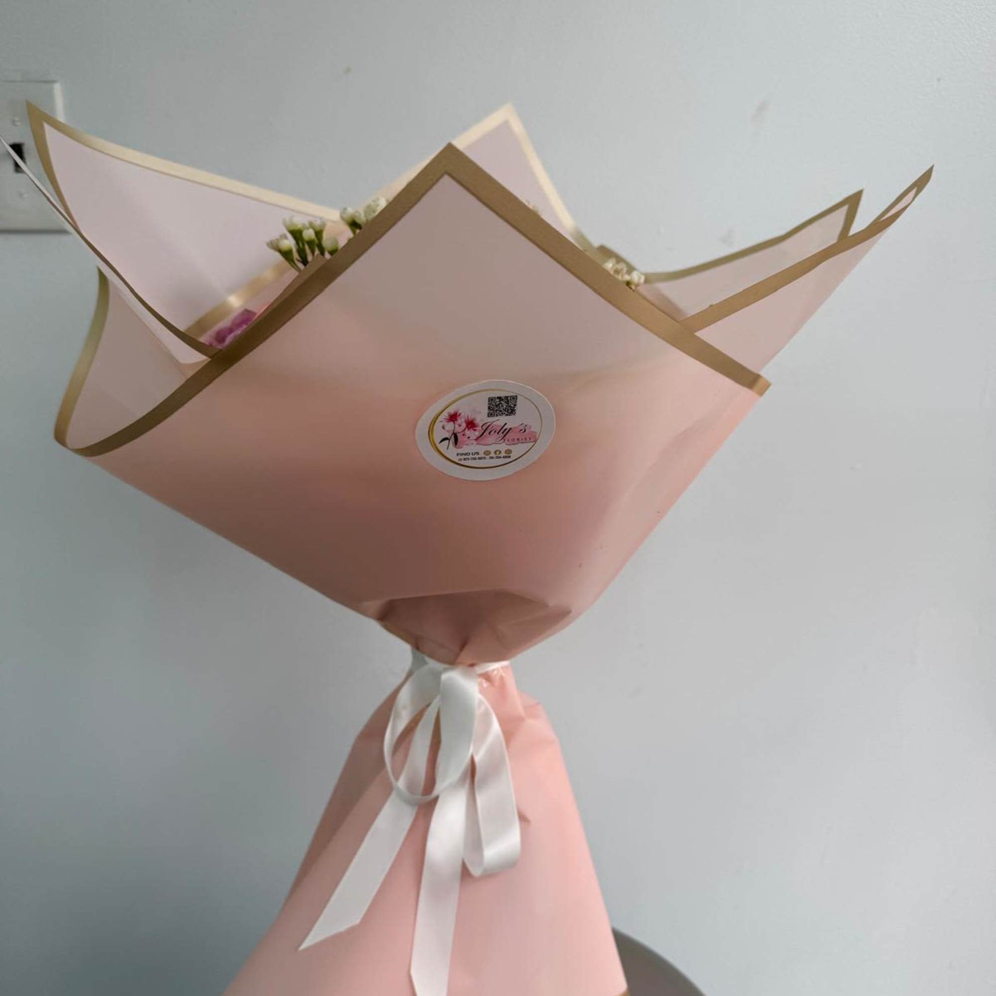 Pink wrapped bouquet with a white ribbon and small white flowers peeking out