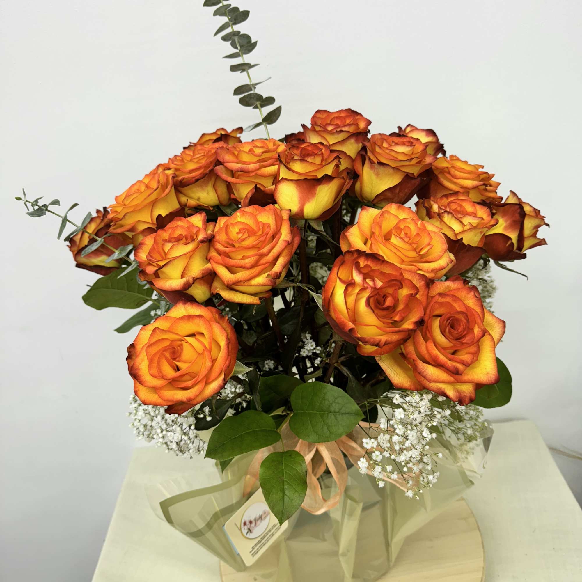 Bouquet of orange and yellow roses with baby's breath in a wrapped container