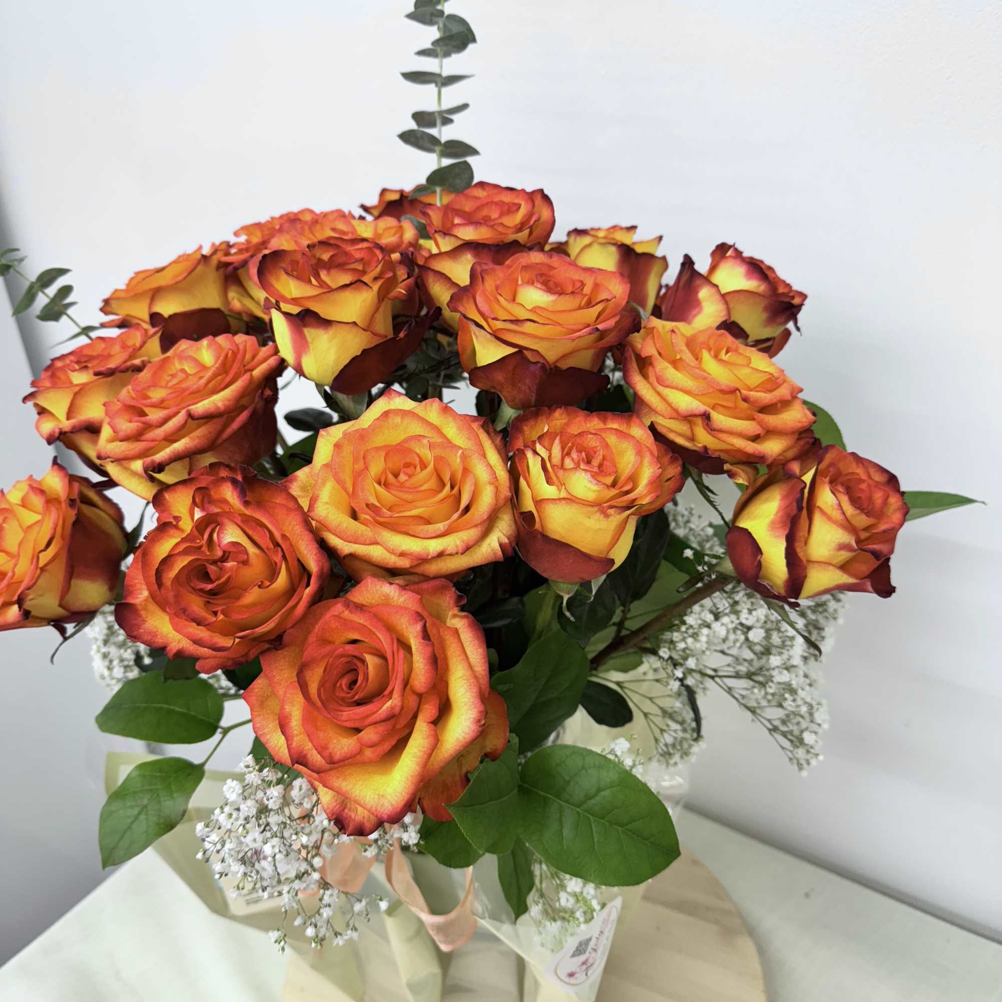 Bouquet of orange and yellow roses with baby's breath in a wrapped vase