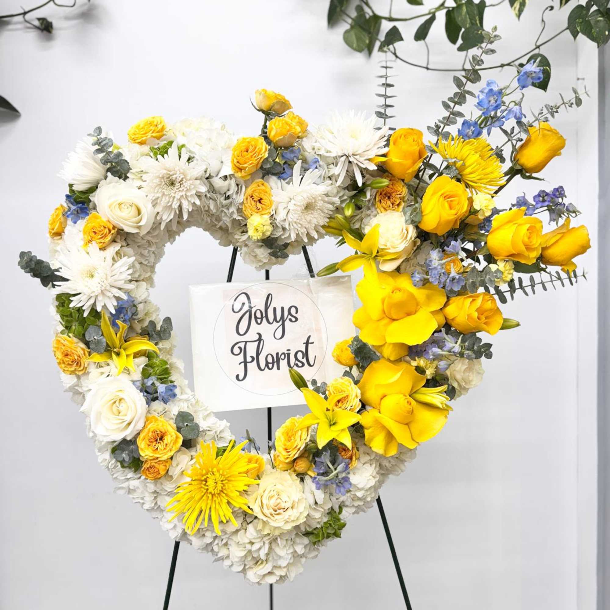 Heart-shaped floral wreath on an easel with yellow, white, and blue flowers