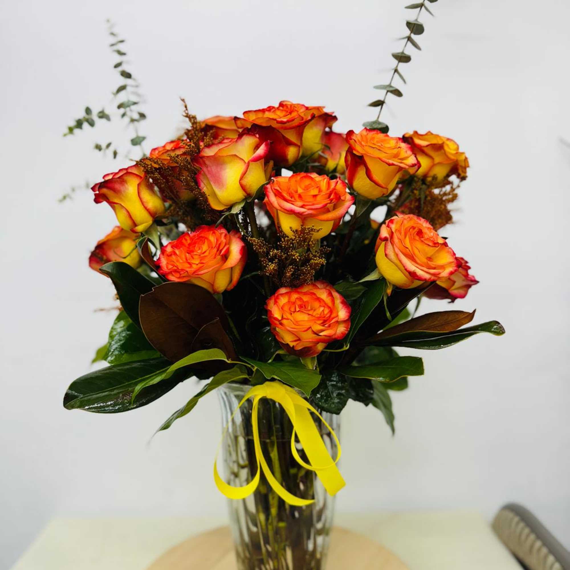 Bouquet of orange and yellow roses in a clear glass vase with a yellow ribbon