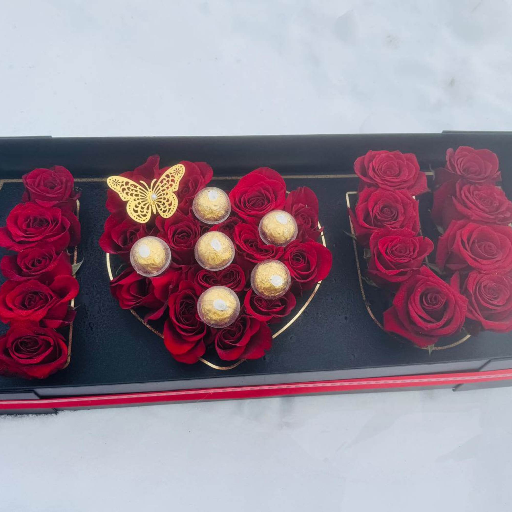 Black gift box with red roses, gold chocolates, and a butterfly decoration