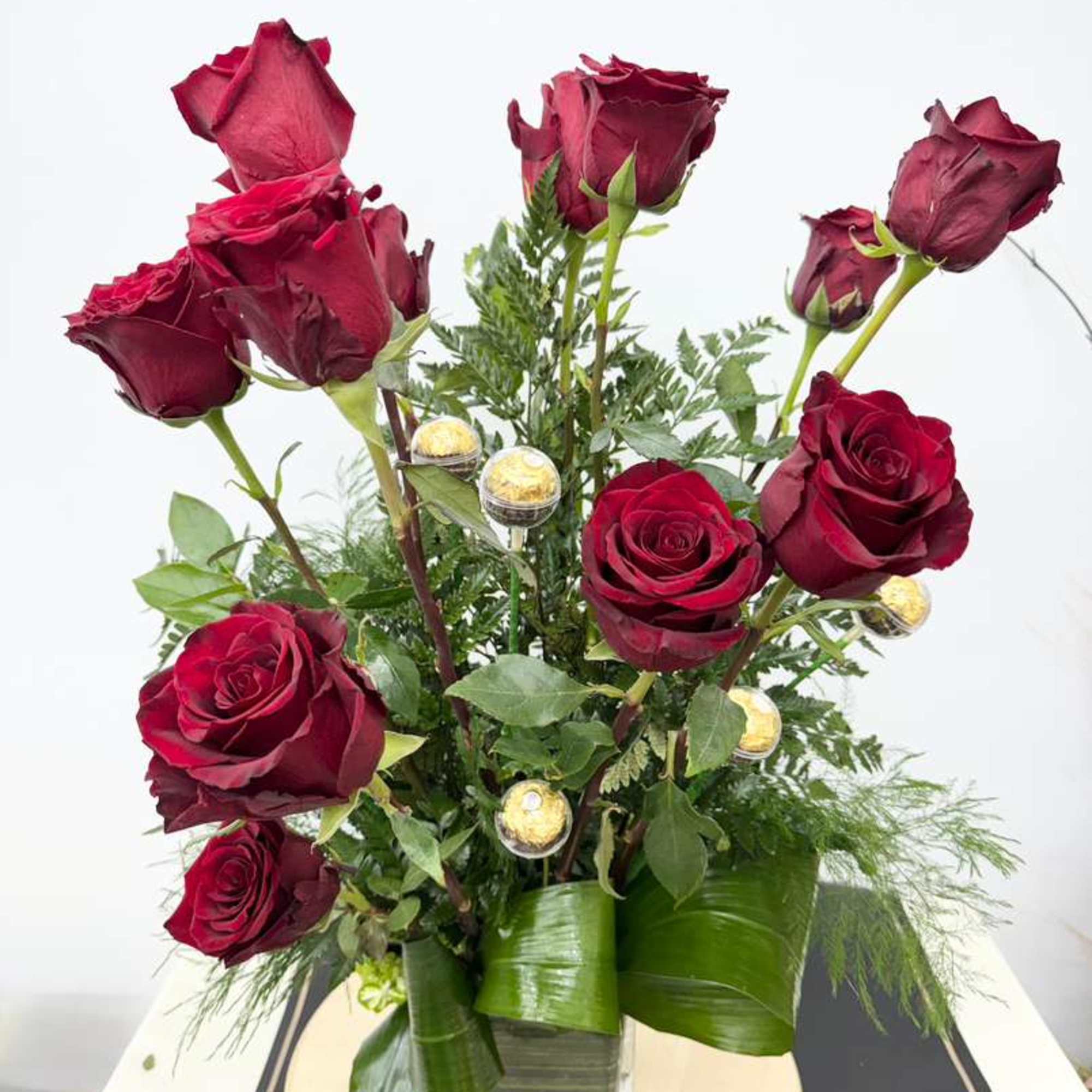 Red roses arranged in a clear square vase with greenery