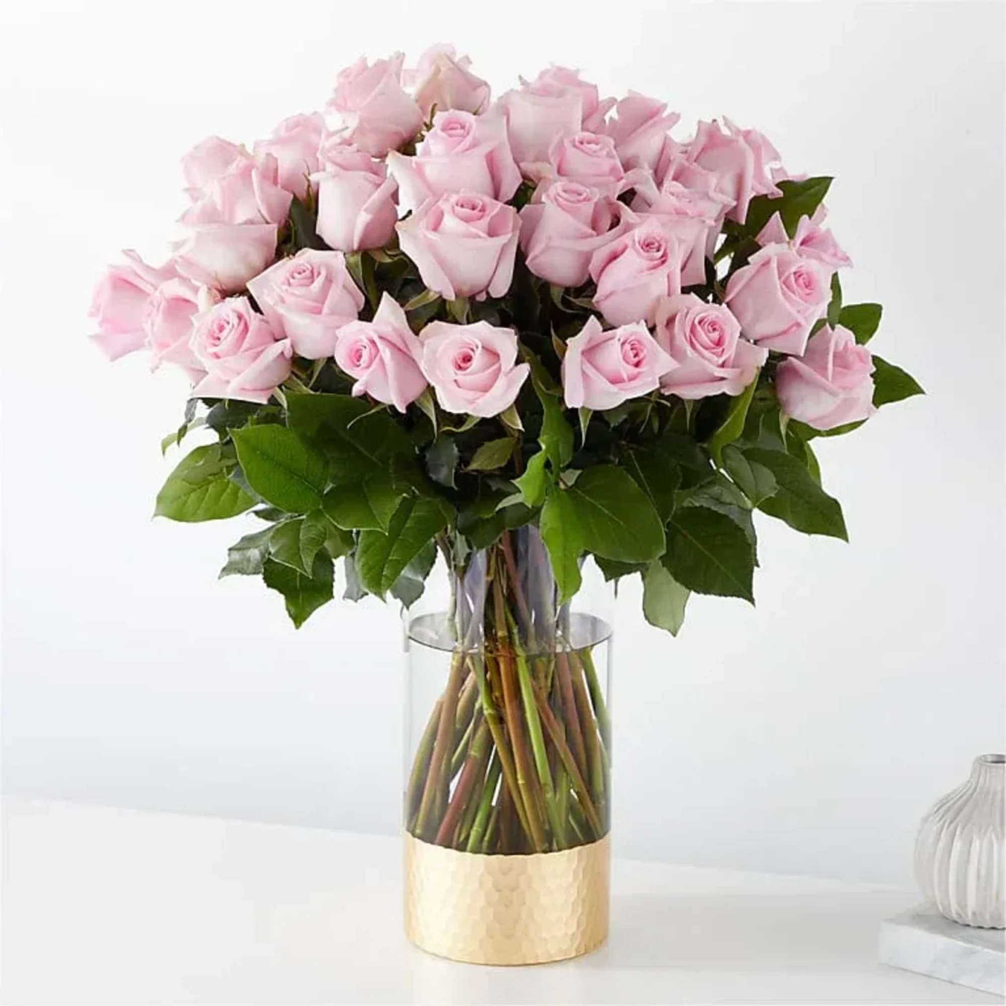 Pink roses arranged in a clear glass vase with a gold base