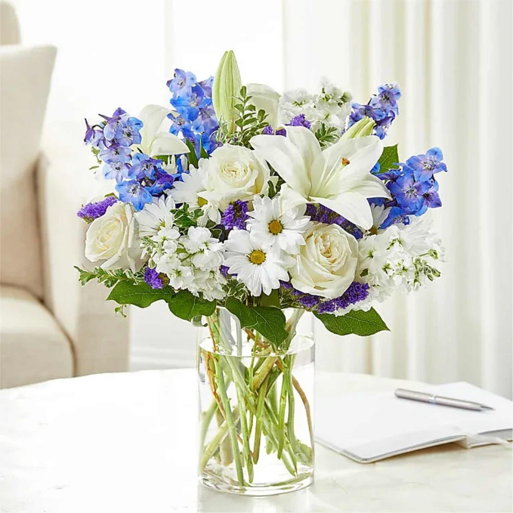 White lilies, roses, and blue flowers in a clear glass vase