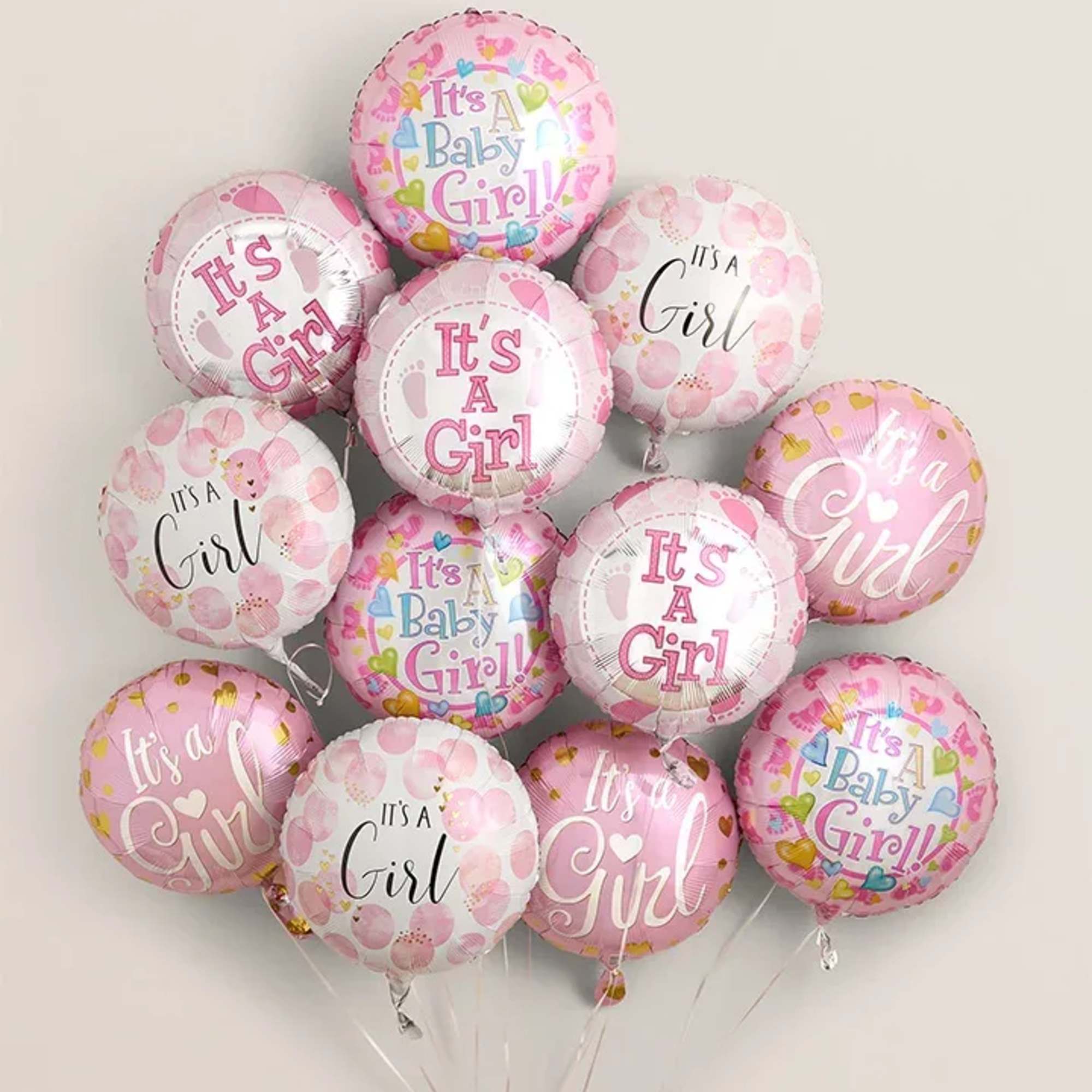 Cluster of pink baby girl balloons against a plain wall