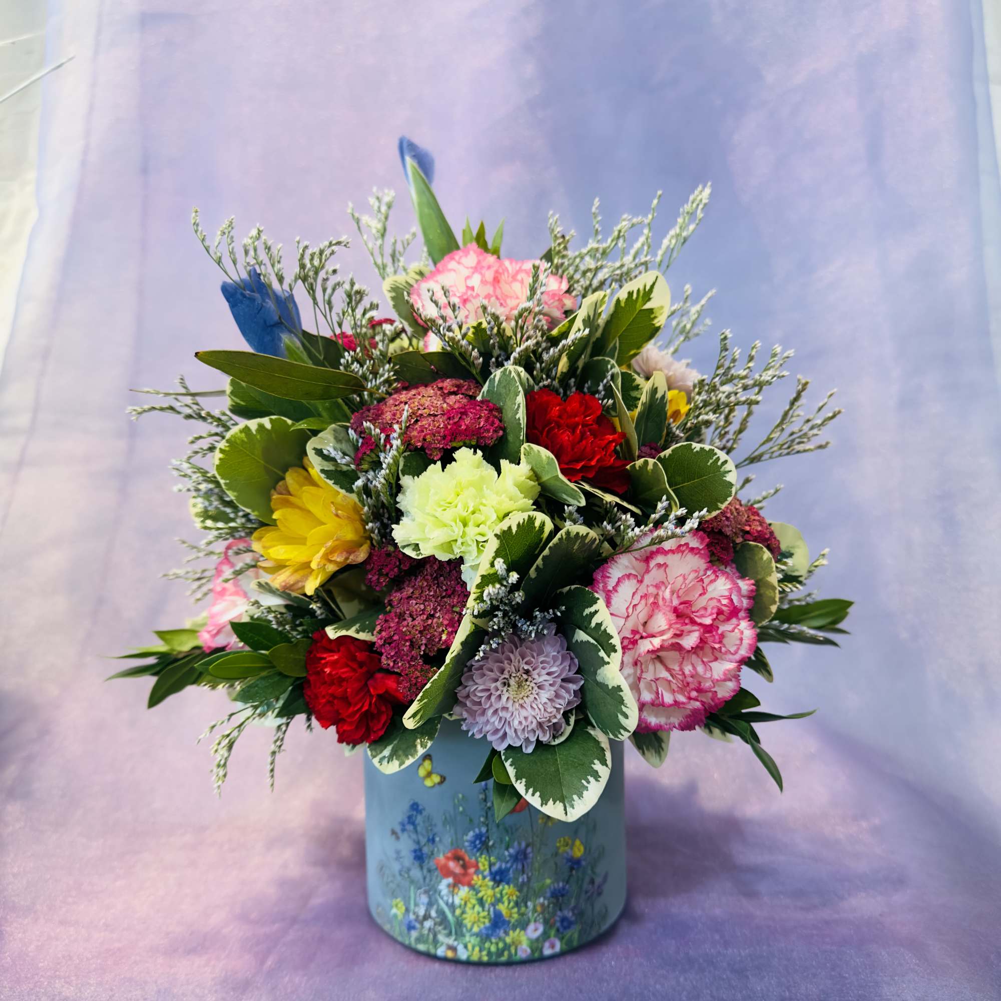 A cheerful garden-style arrangement featuring pink and red carnations, pale lavender accents