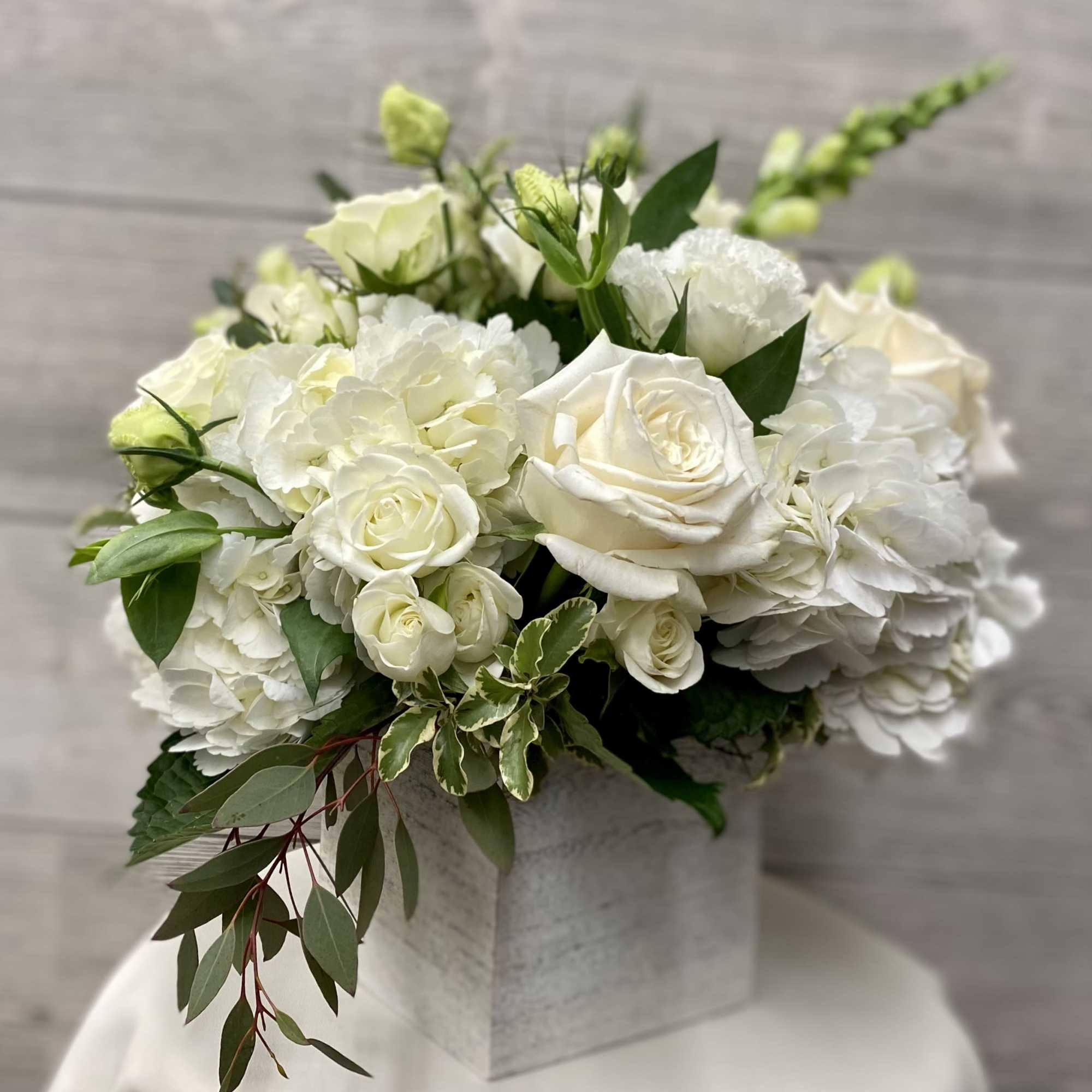 White roses and hydrangeas arranged in a square box with greenery