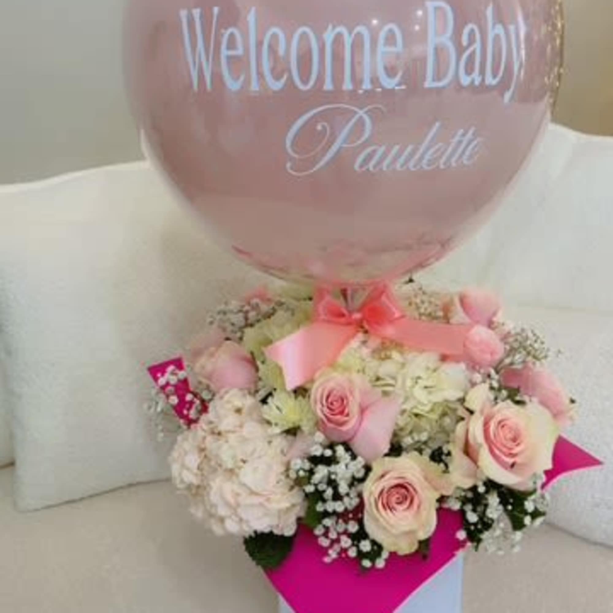 Pink balloon above a pastel flower arrangement with a baby name message