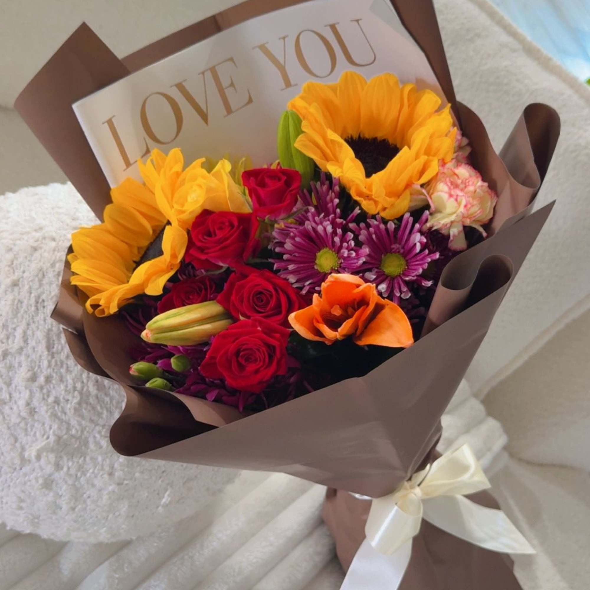 A vibrant mix of sunflowers, roses, and seasonal blooms wrapped in elegant