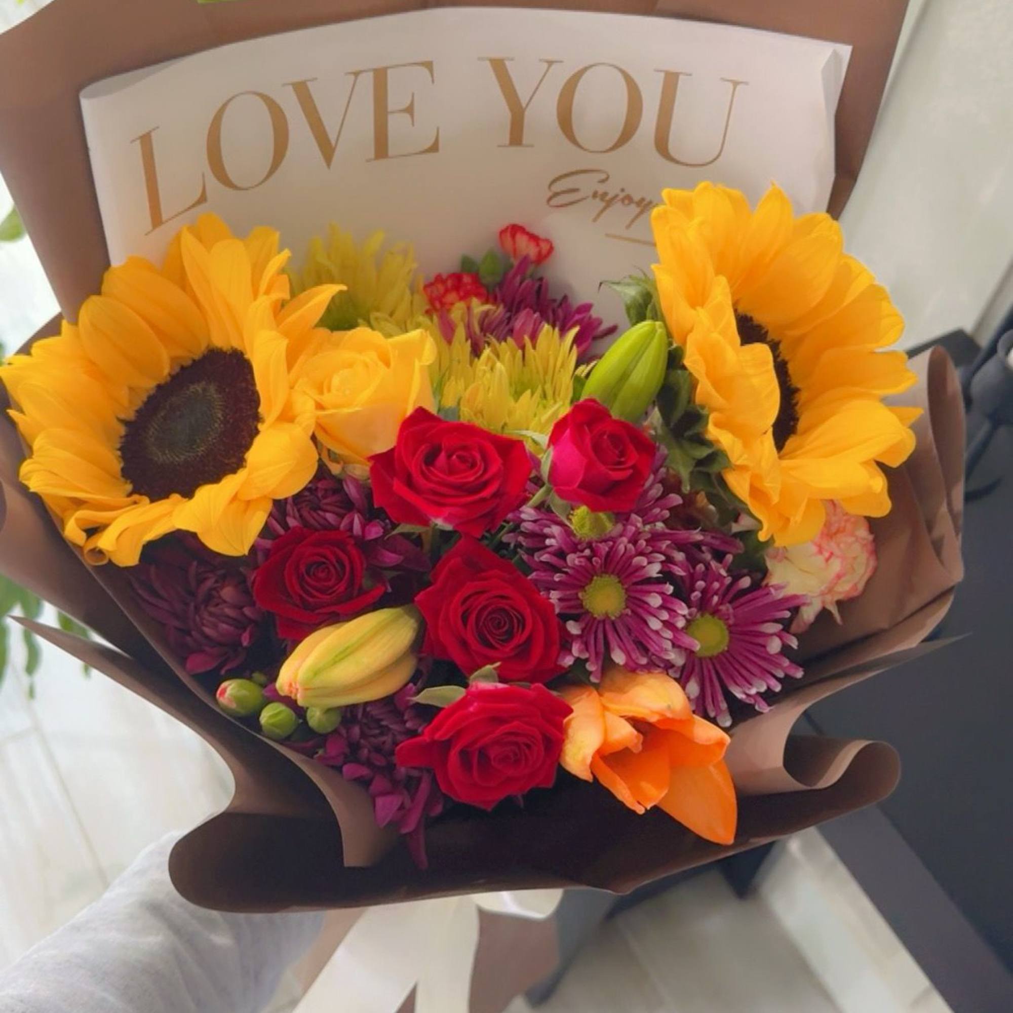 A vibrant mix of sunflowers, roses, and seasonal blooms wrapped in elegant