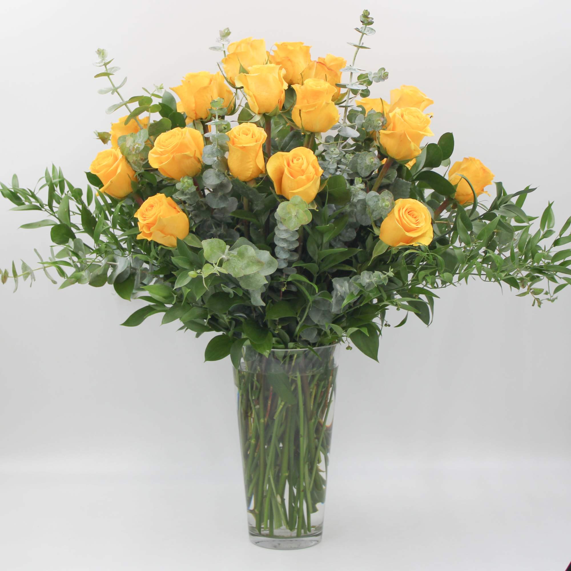 Yellow roses in a clear glass vase with greenery