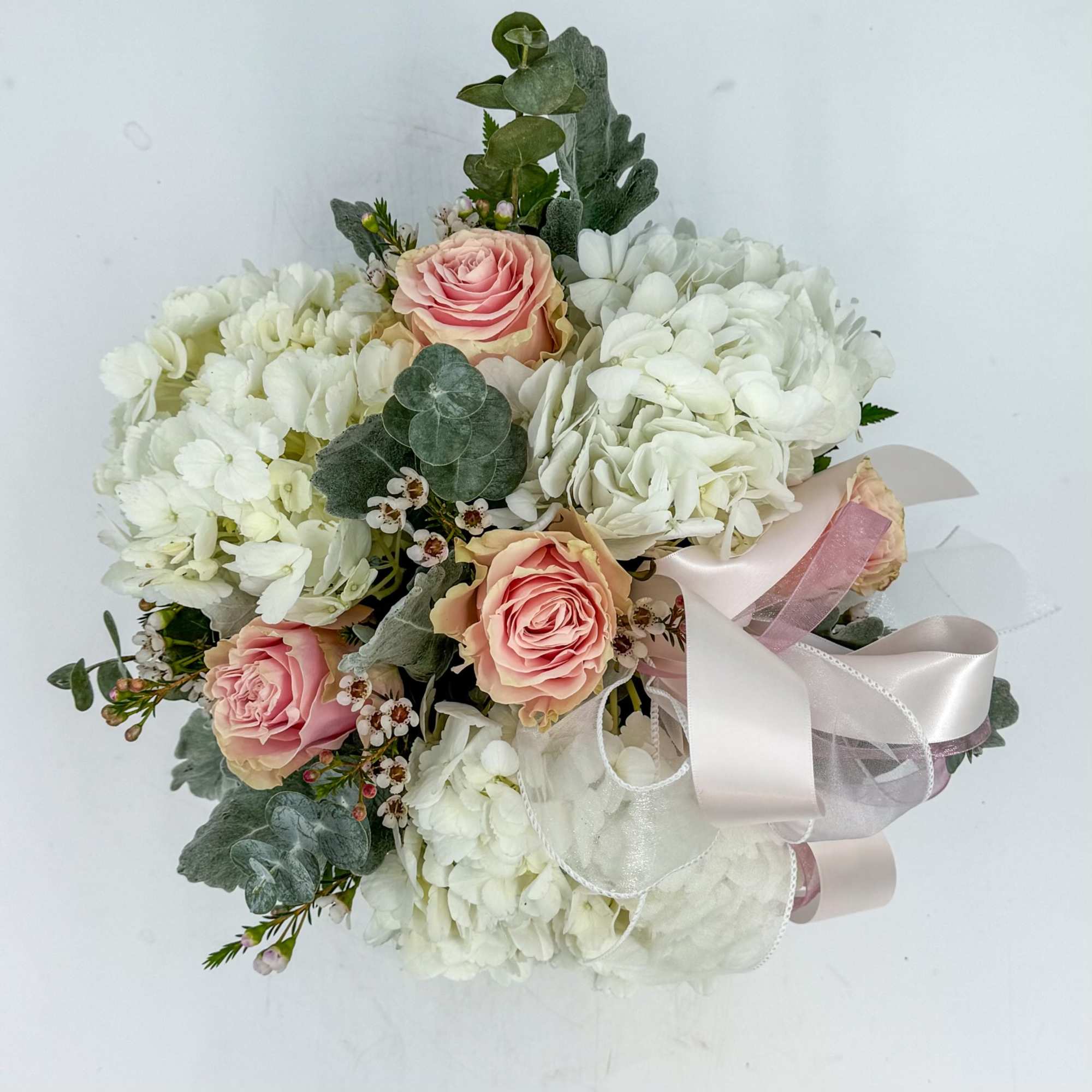 Compact bouquet of white hydrangeas and blush roses with pastel ribbon bow