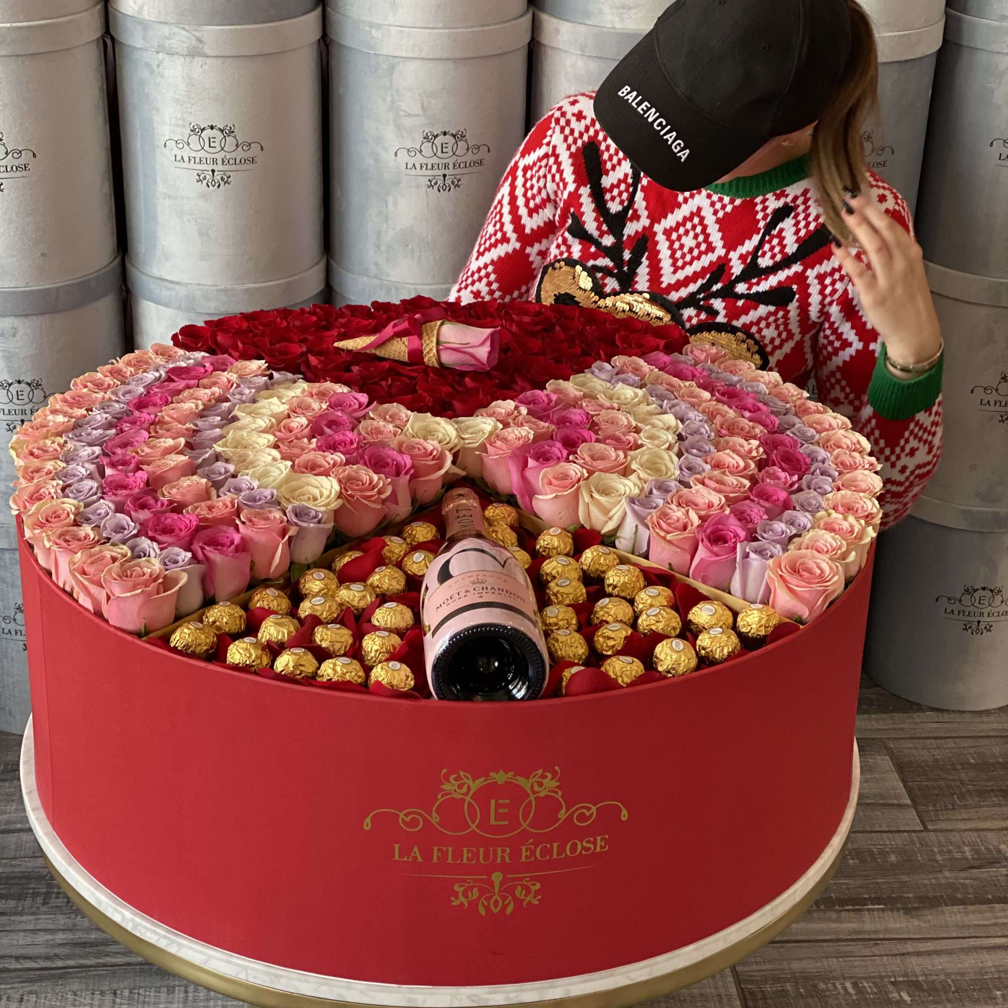 Heart-shaped rose arrangement with chocolates and a champagne bottle in a red box