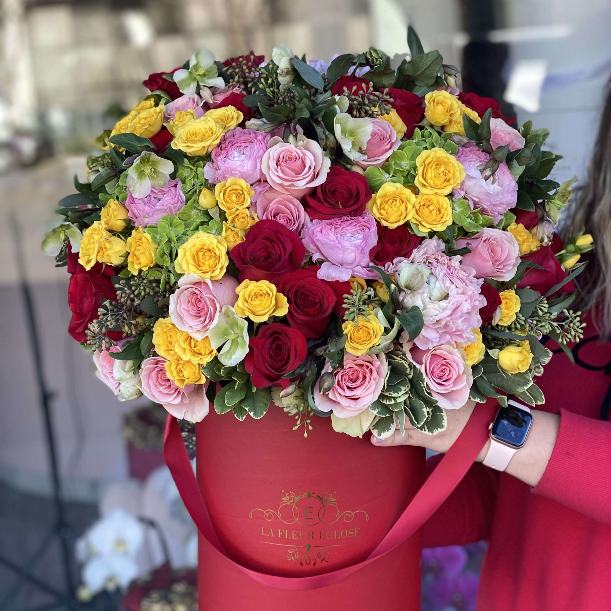 Large bouquet of pink, red, and yellow roses in a red hatbox
