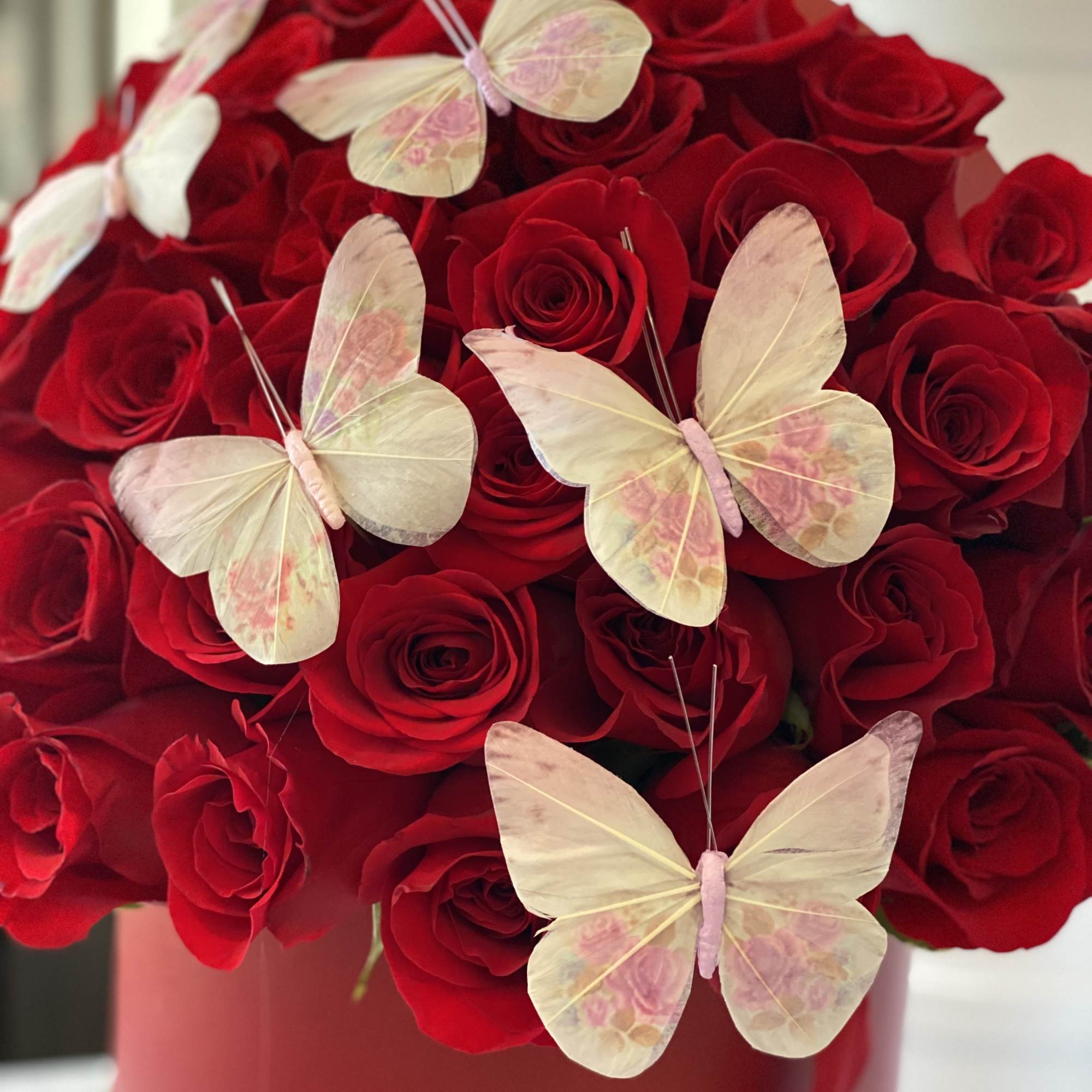 Red roses with pale butterfly decorations in a pink vase