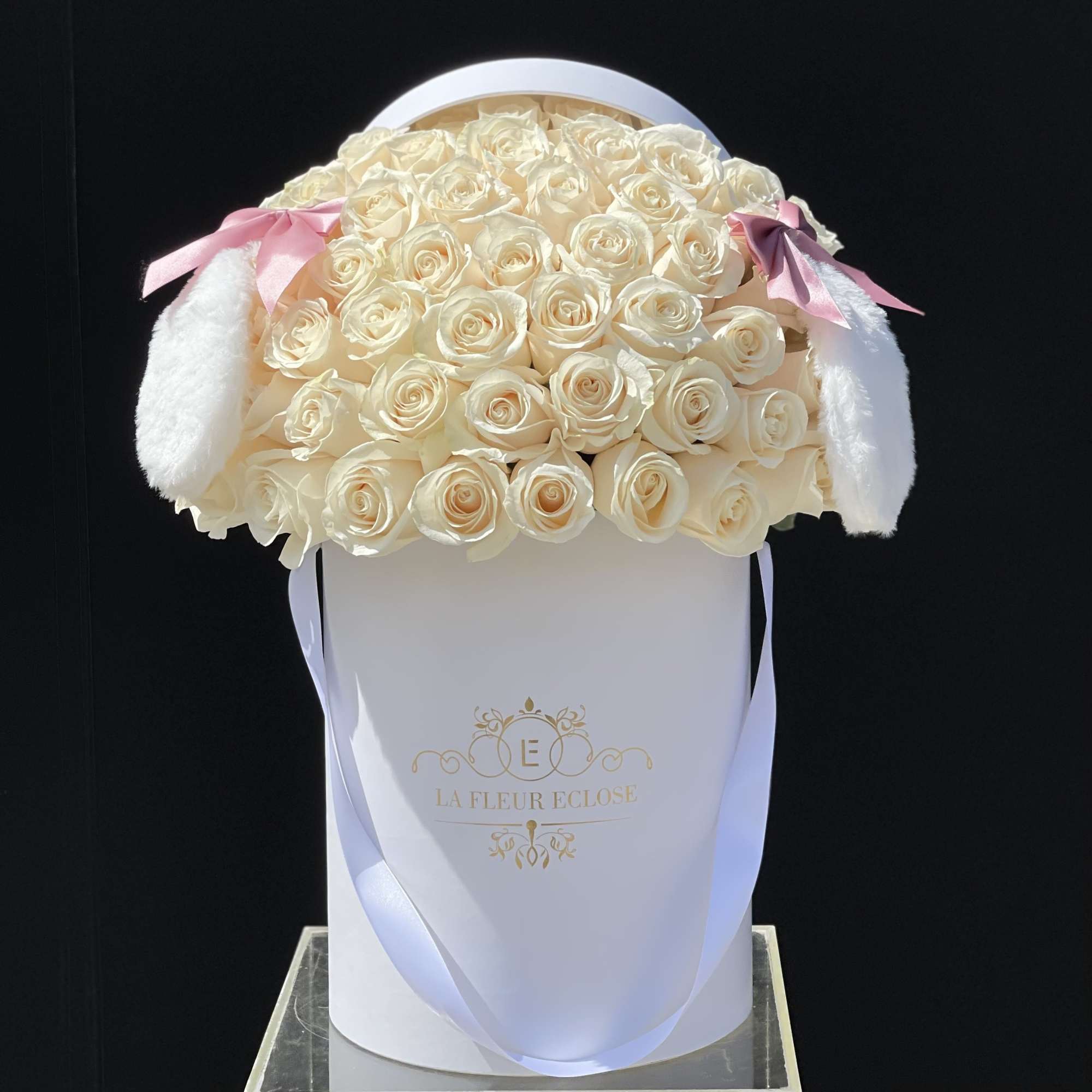 Large arrangement of cream roses in a white hat box with pink bows and plush bunny ear accents