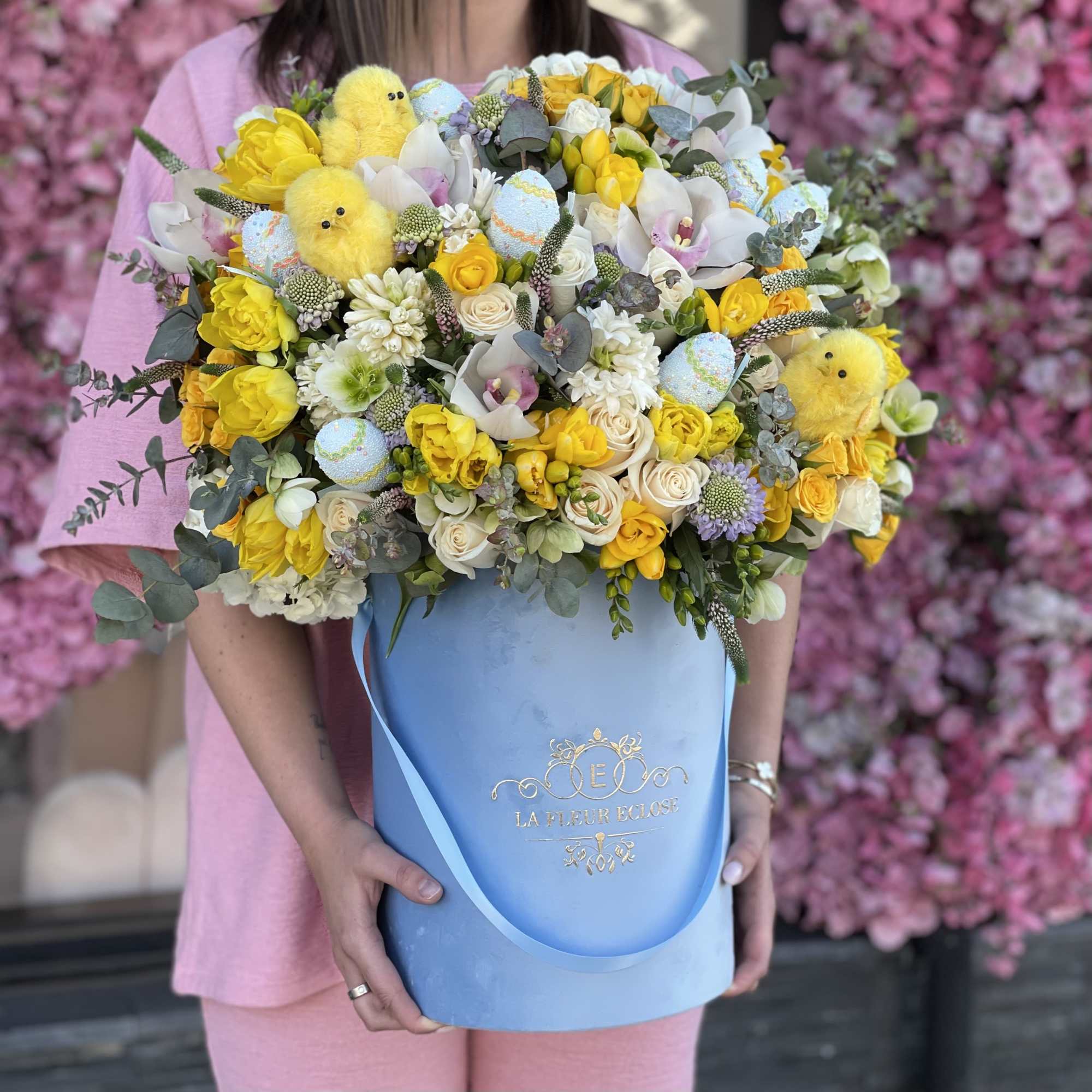 Large yellow and white flower arrangement in a blue hatbox with chick decorations