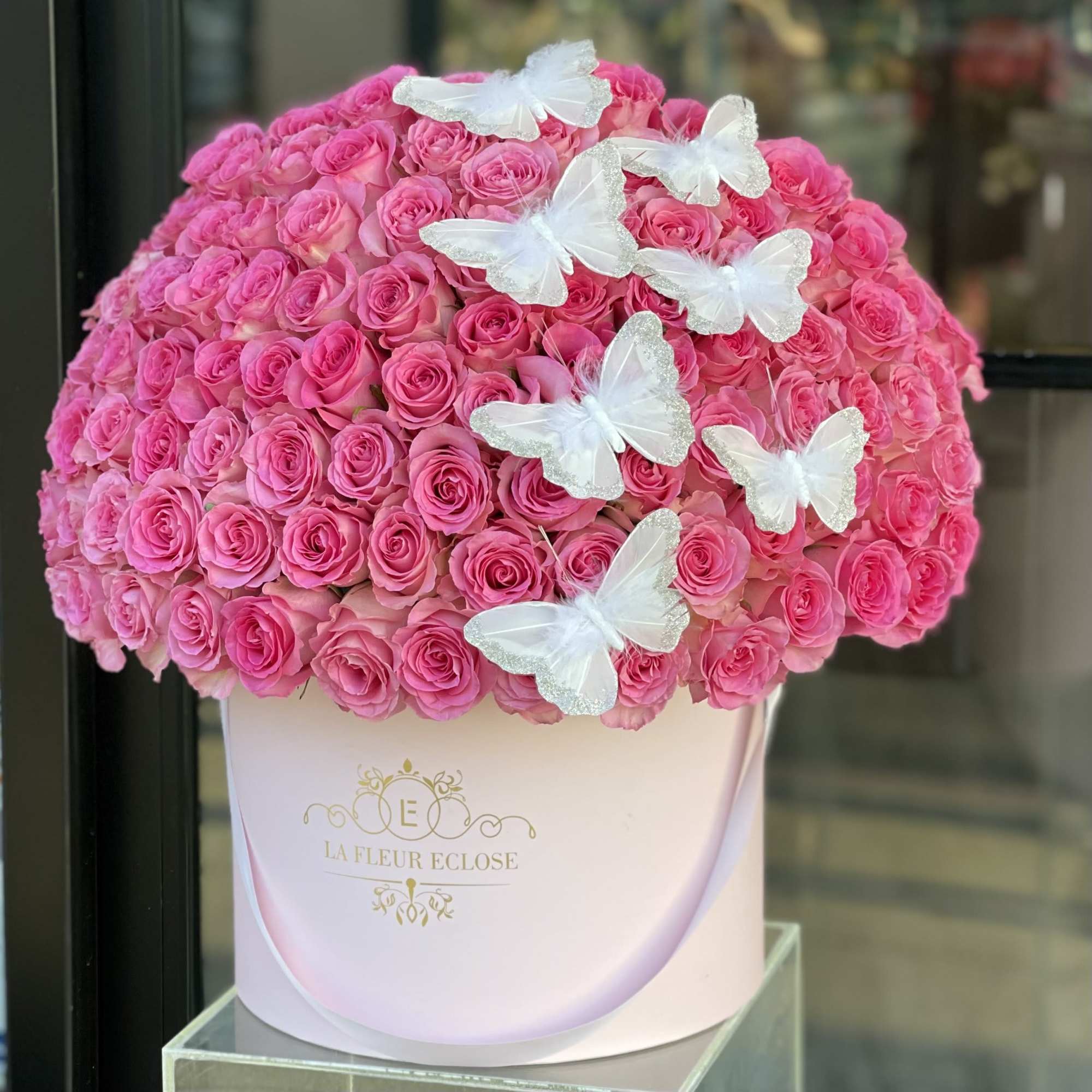 Large pink rose arrangement in a white hat box with white butterfly decorations