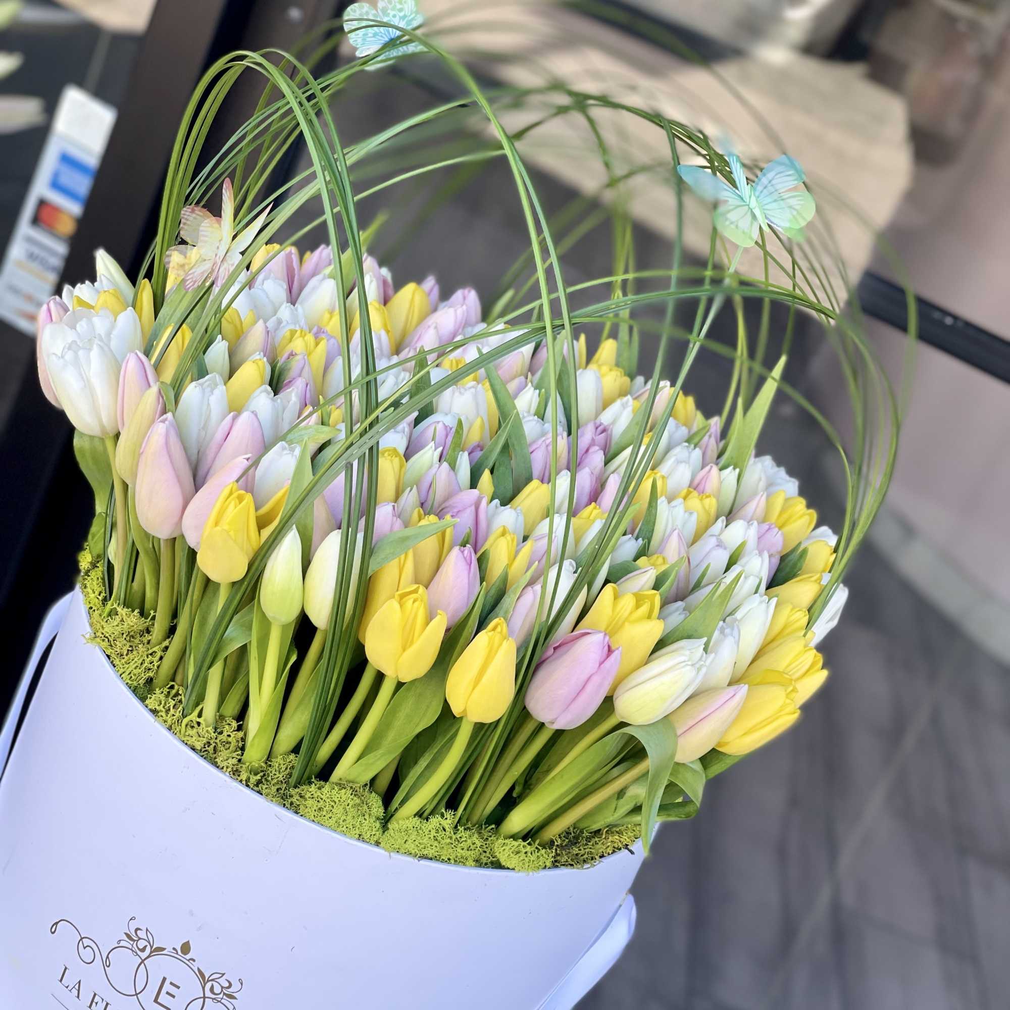 Bouquet of pastel tulips in a white hatbox with butterfly picks