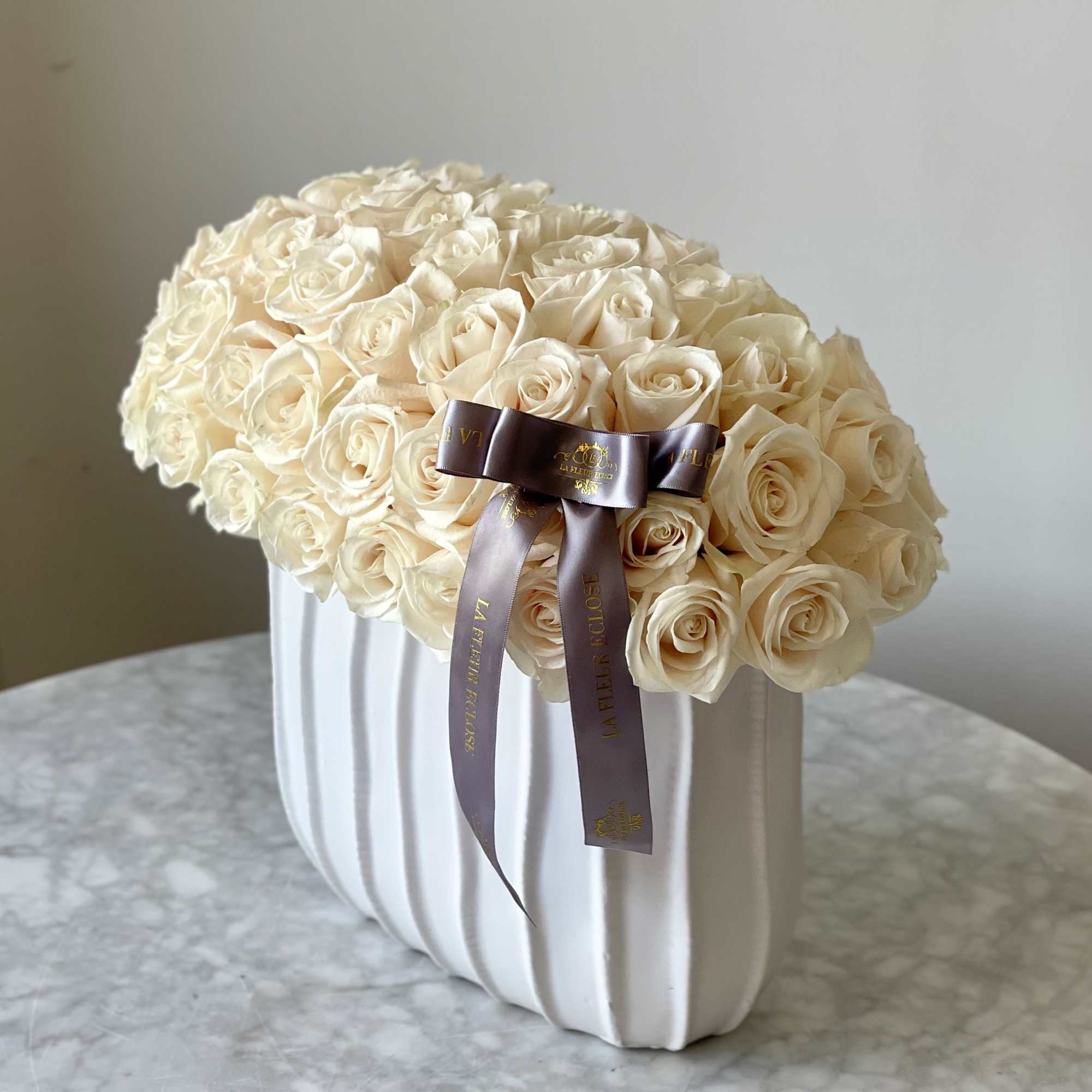Cream rose arrangement in a white ribbed vase with a satin ribbon