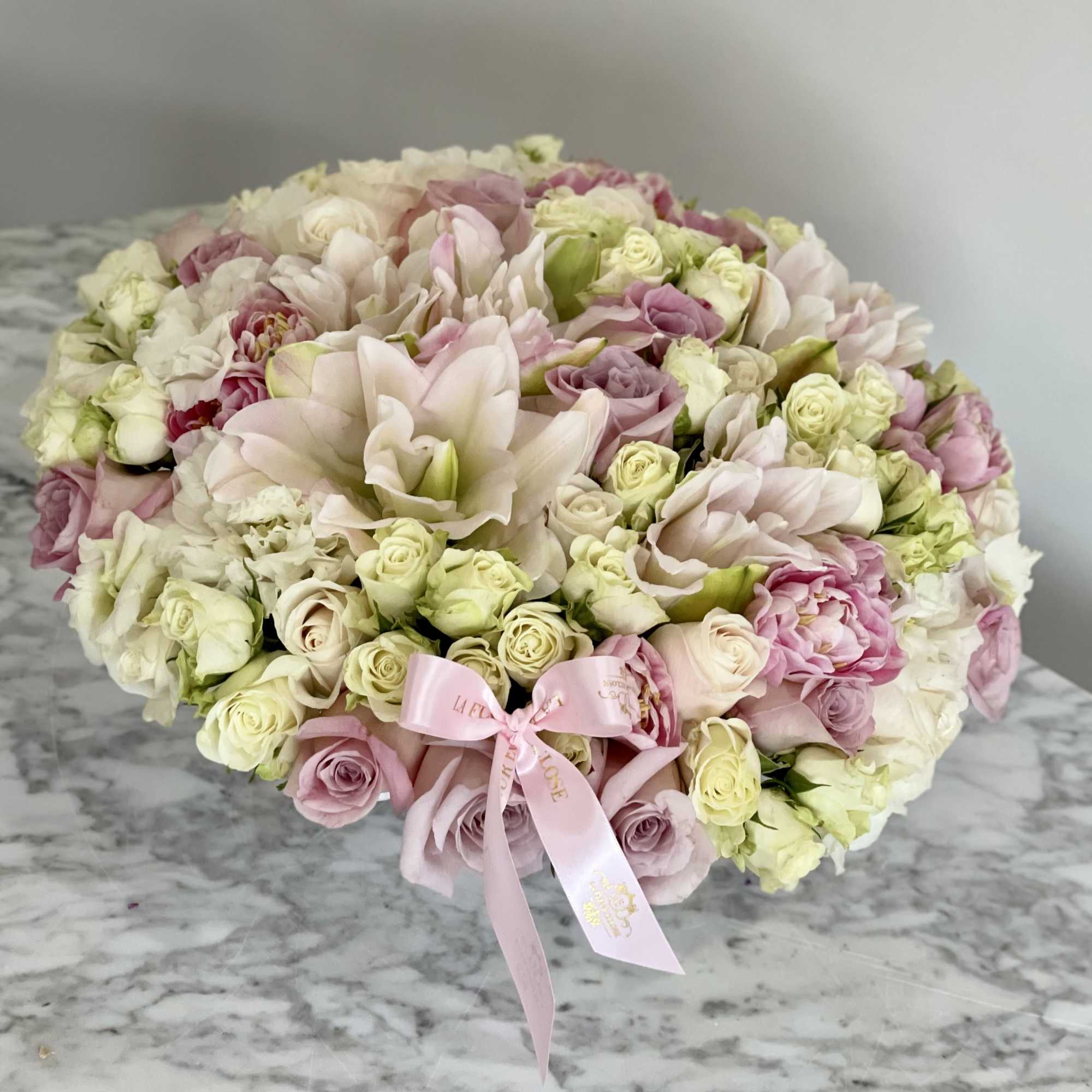 Round bouquet of pale pink and cream roses with a pink ribbon