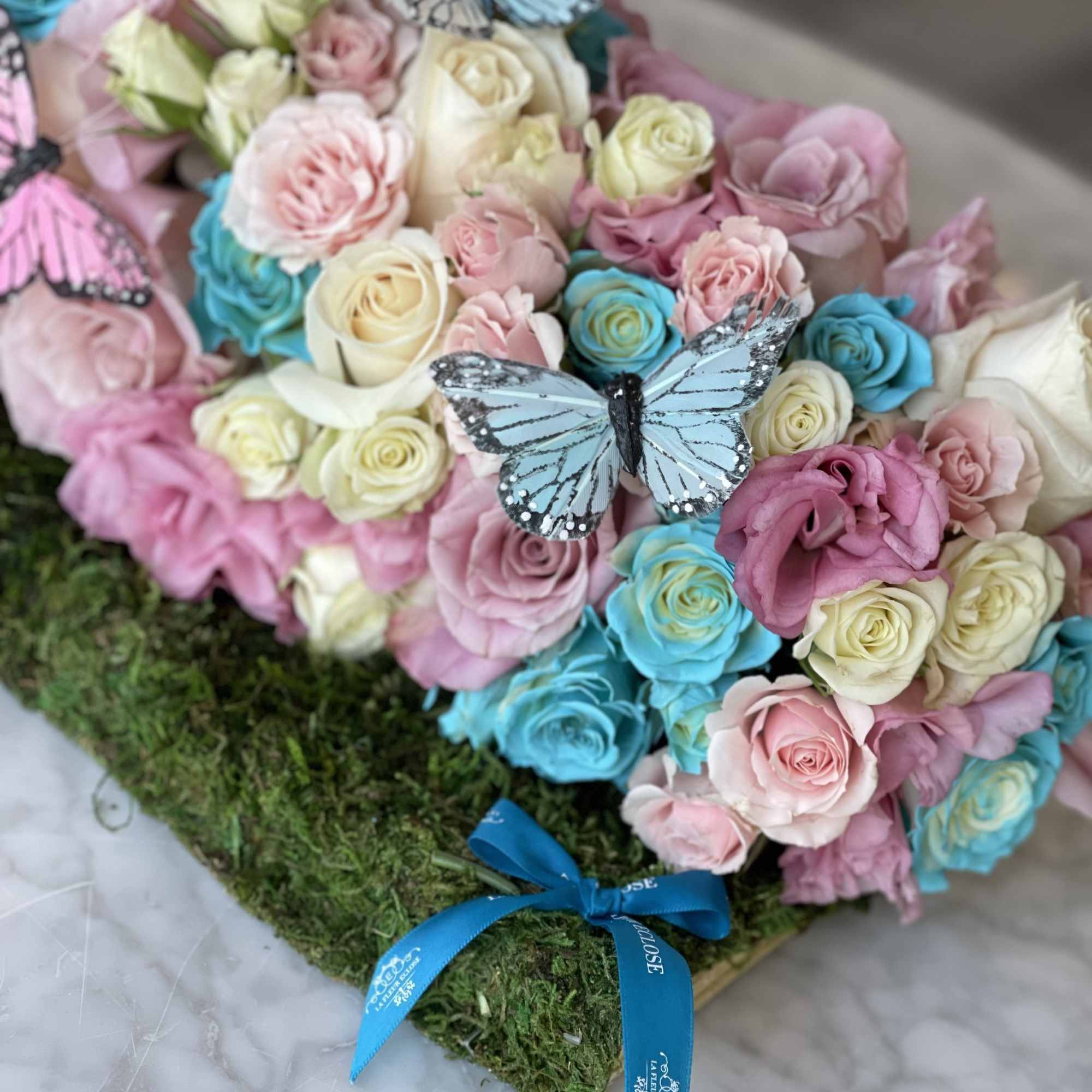 Pastel rose arrangement with butterfly decorations on a moss base