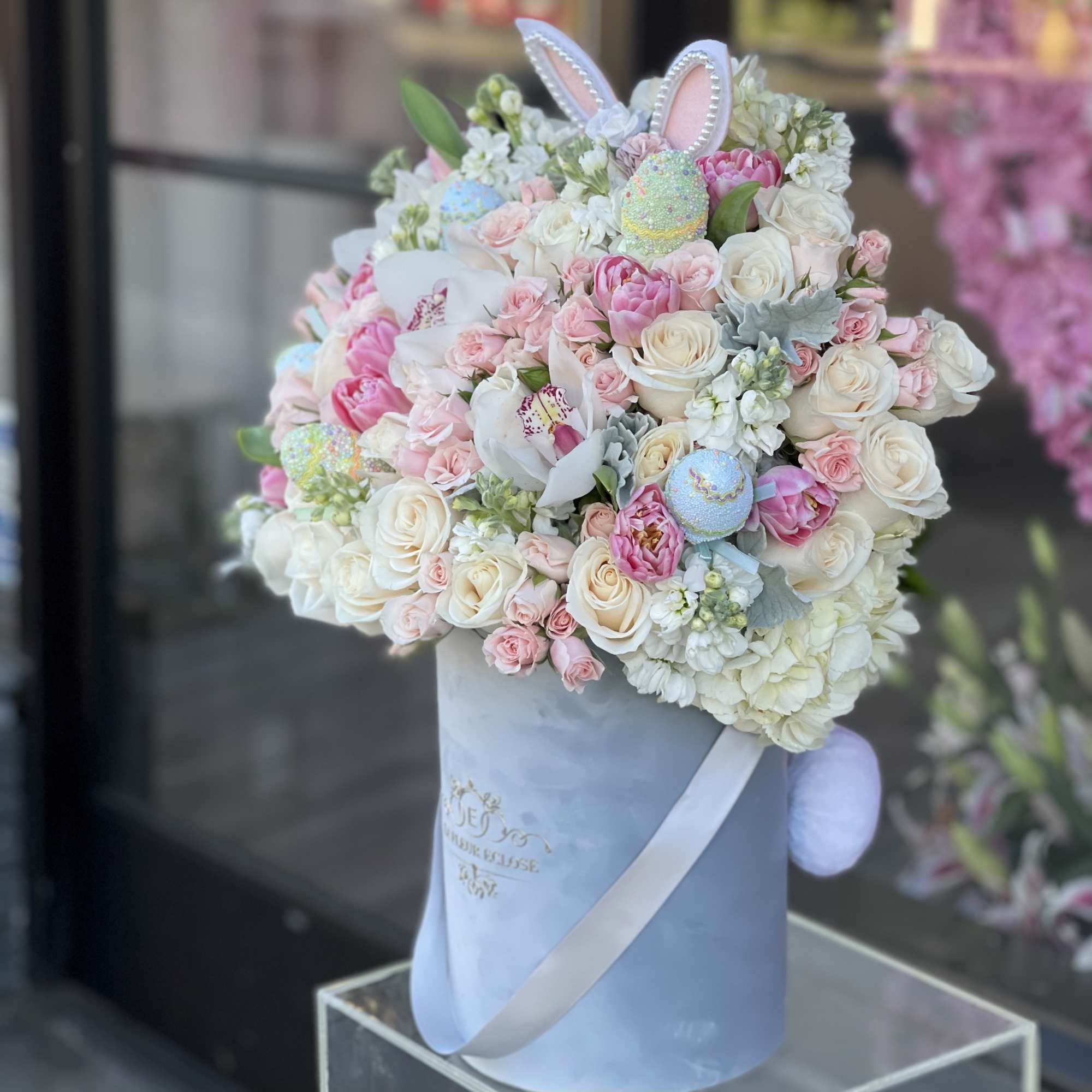 Pastel bouquet of roses and orchids in a blue hatbox with bunny ears