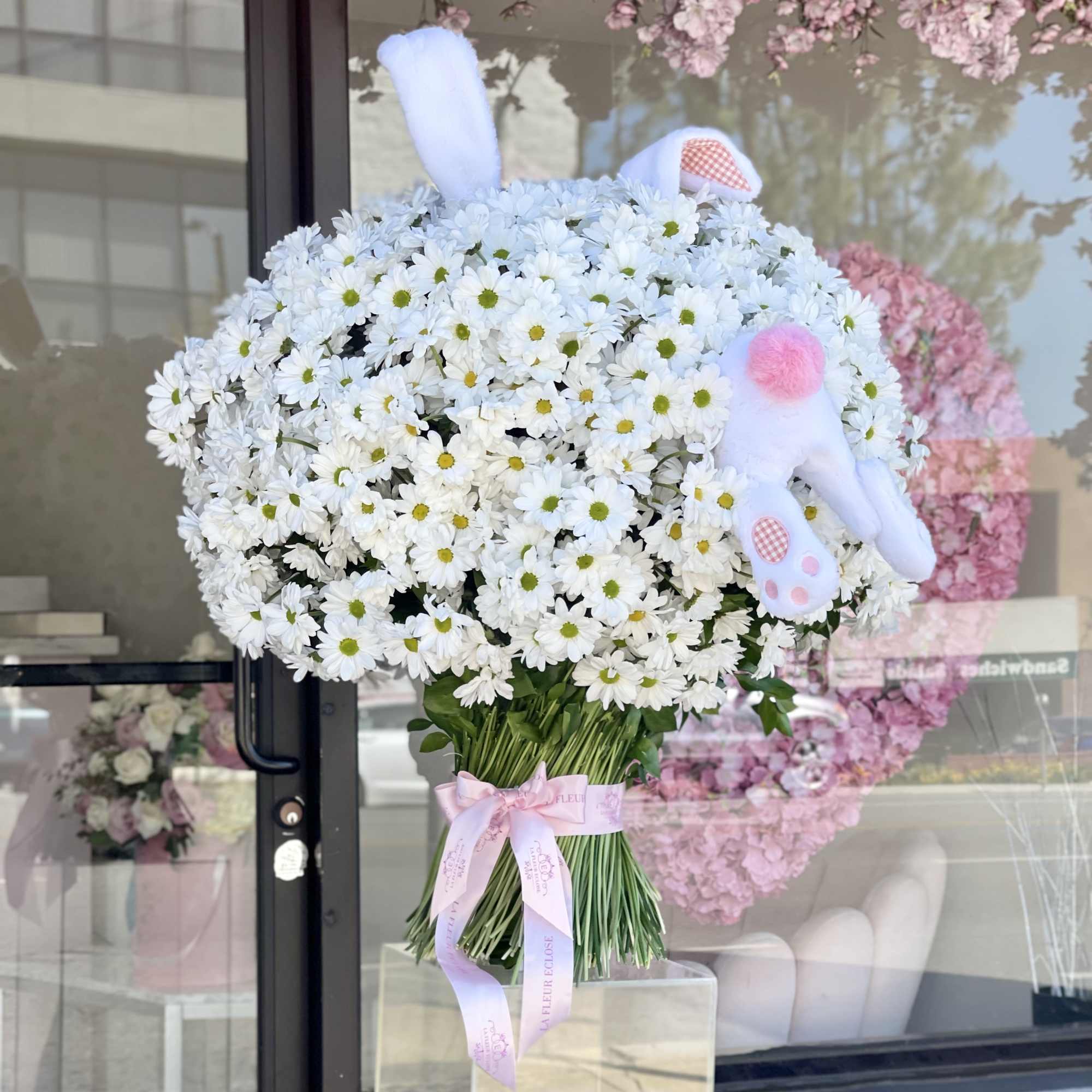Large bouquet of white daisies with pastel bunny decorations and a pink ribbon