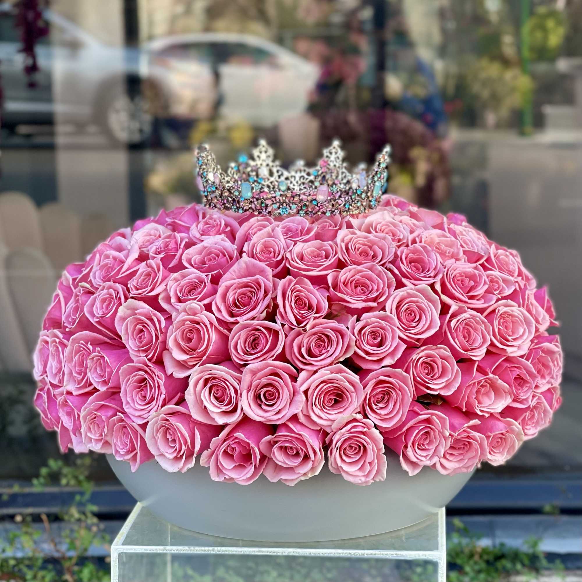 Pink rose arrangement topped with a jeweled crown in a white bowl