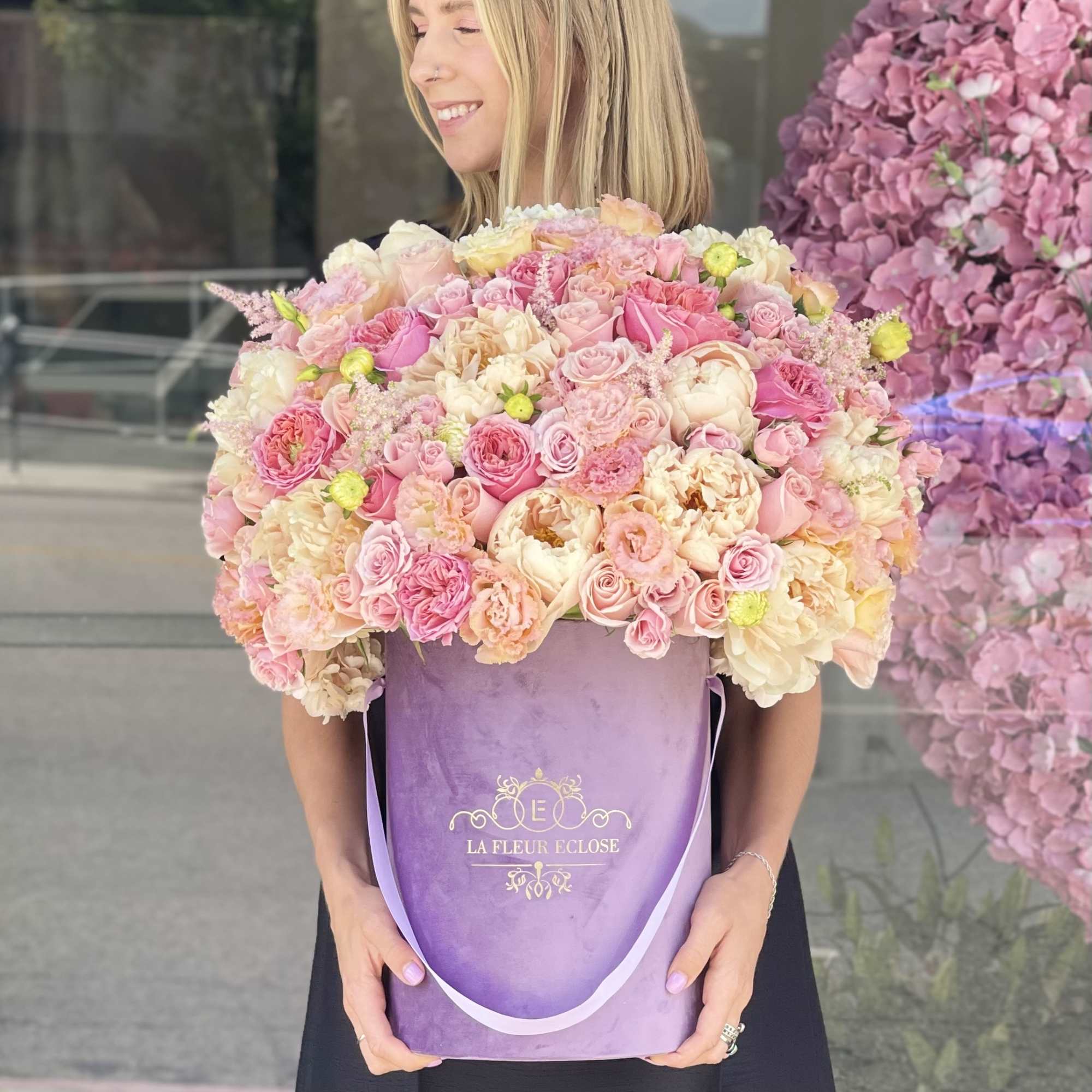 Woman holding a large pastel pink and cream rose bouquet in a purple box
