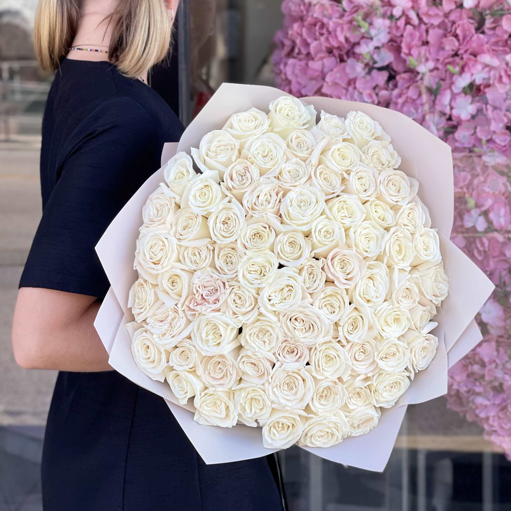Woman holding a large bouquet of white roses wrapped in pale paper
