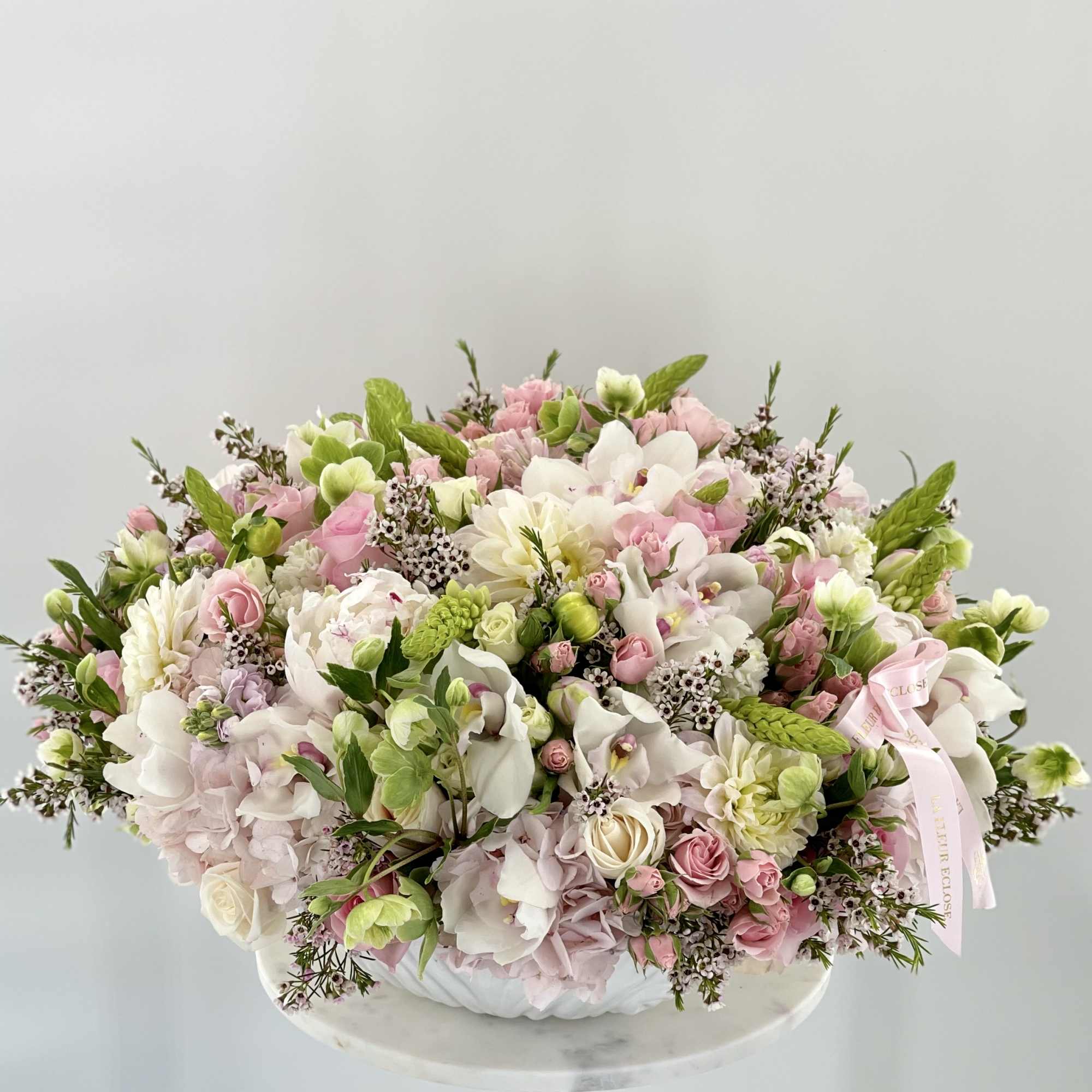 Large pastel flower arrangement in a white container with a pink ribbon