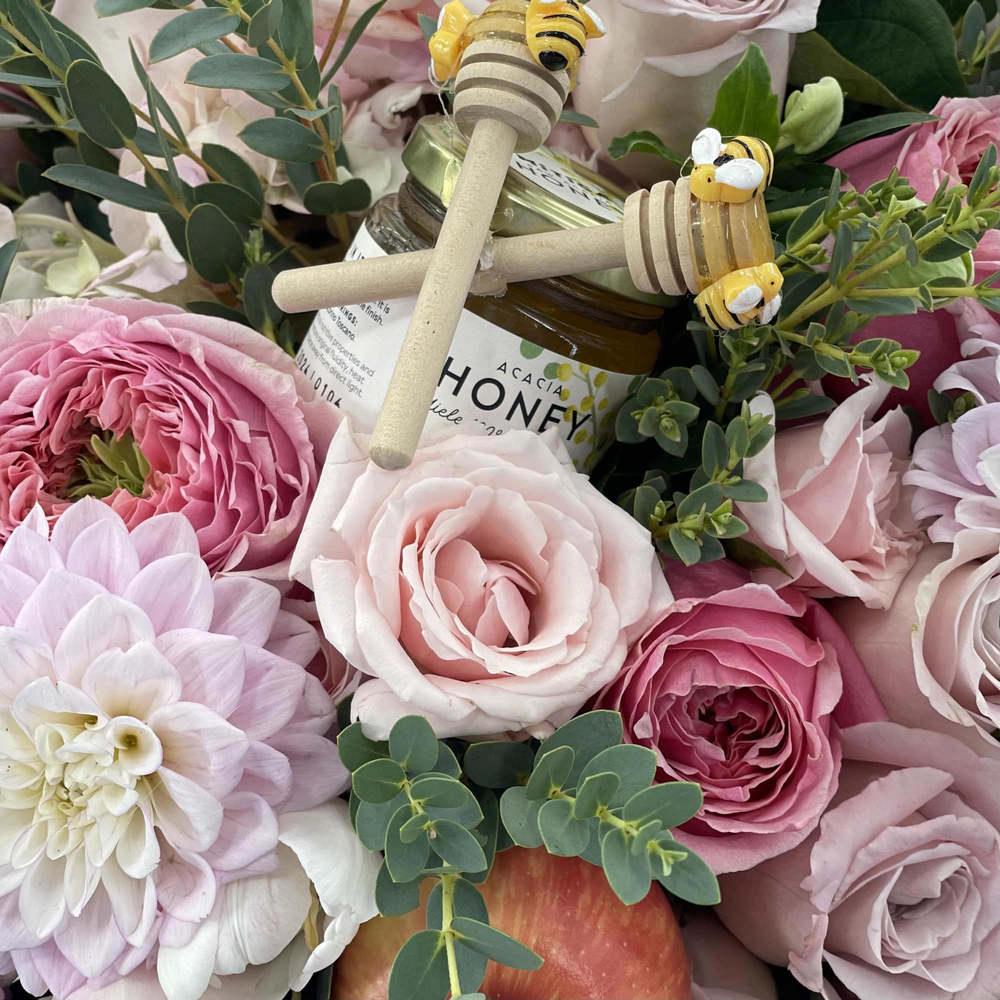 Pink roses and a honey jar with bee toppers in a floral arrangement