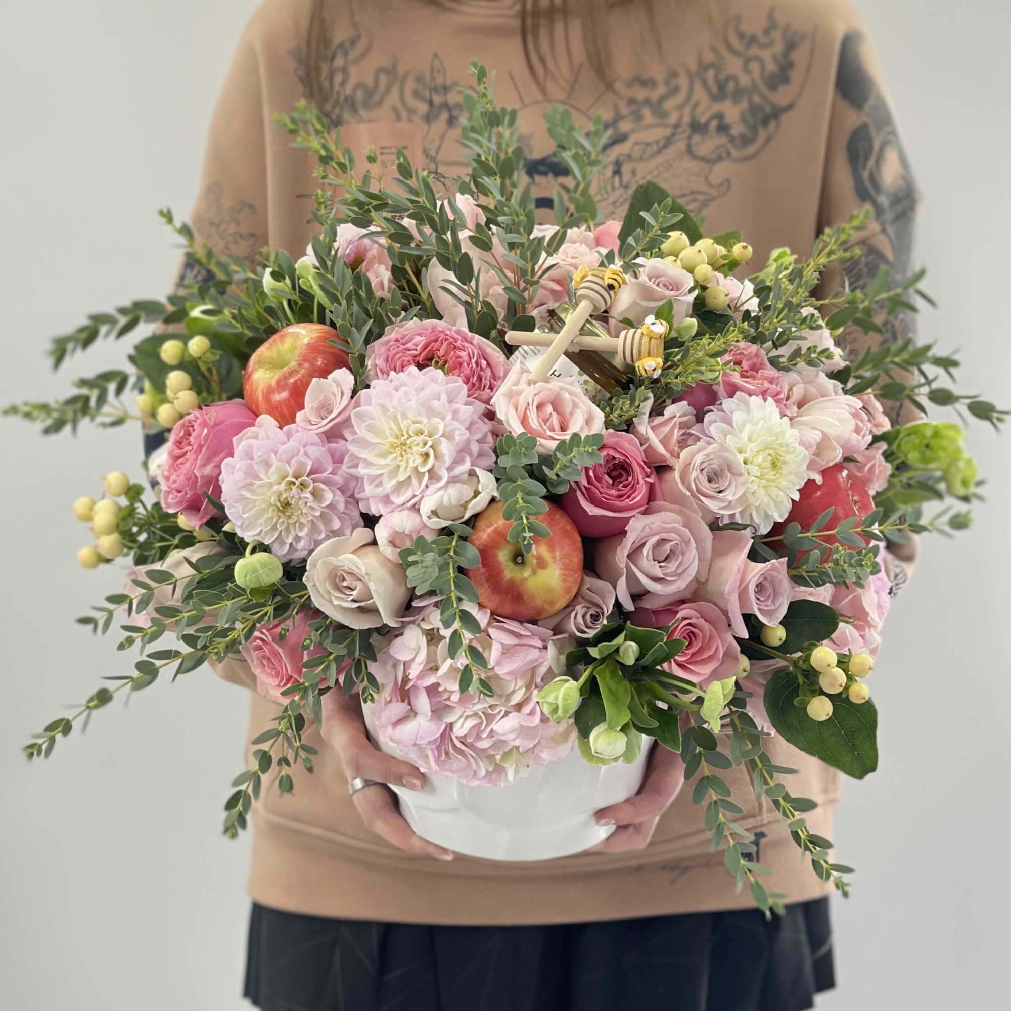 Pink floral arrangement in a white container with apples and greenery