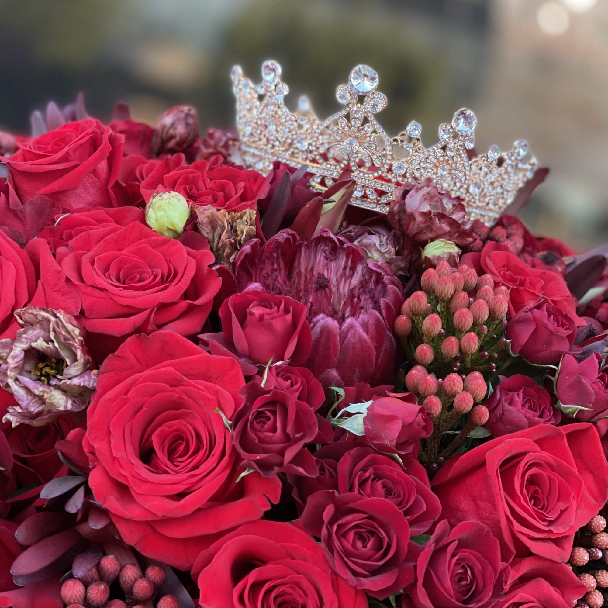 Red roses and burgundy flowers topped with a jeweled crown