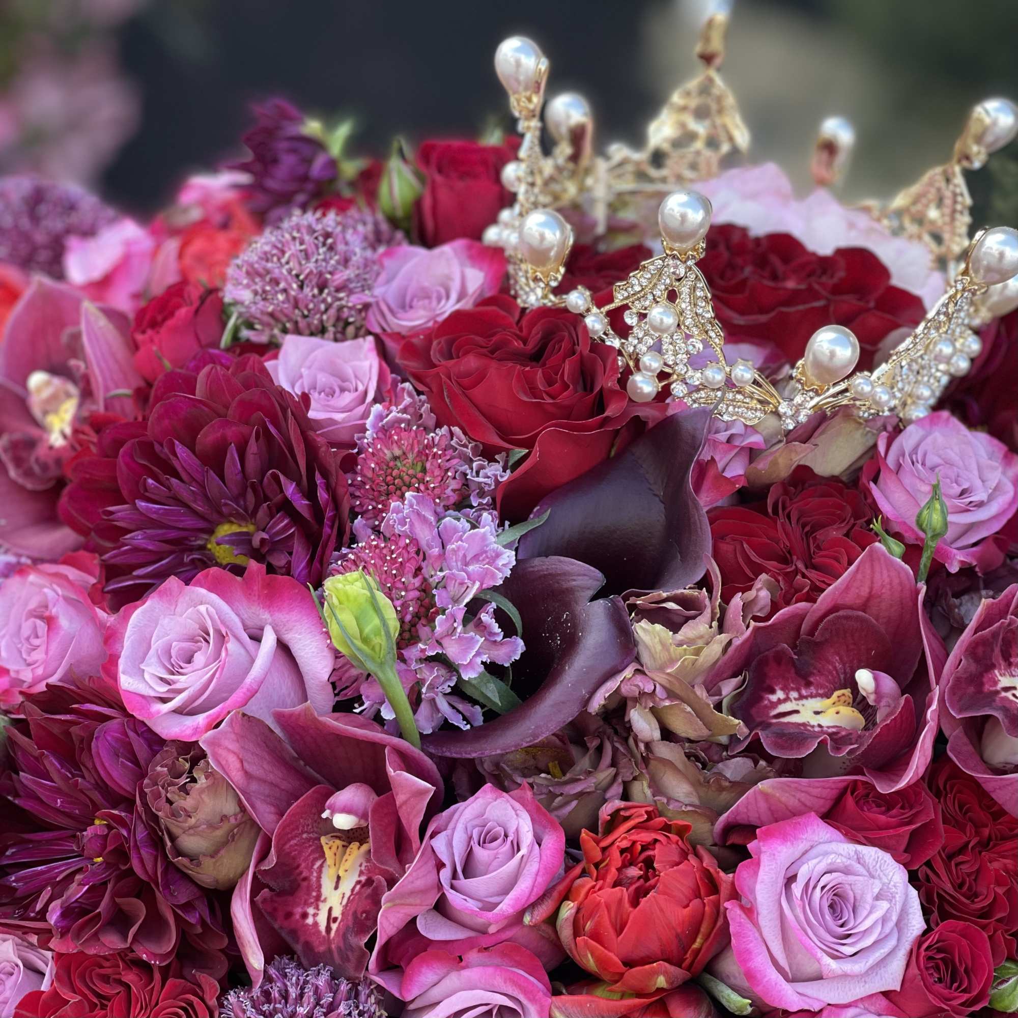 Pink and red bouquet with roses, orchids, and jeweled crown accents