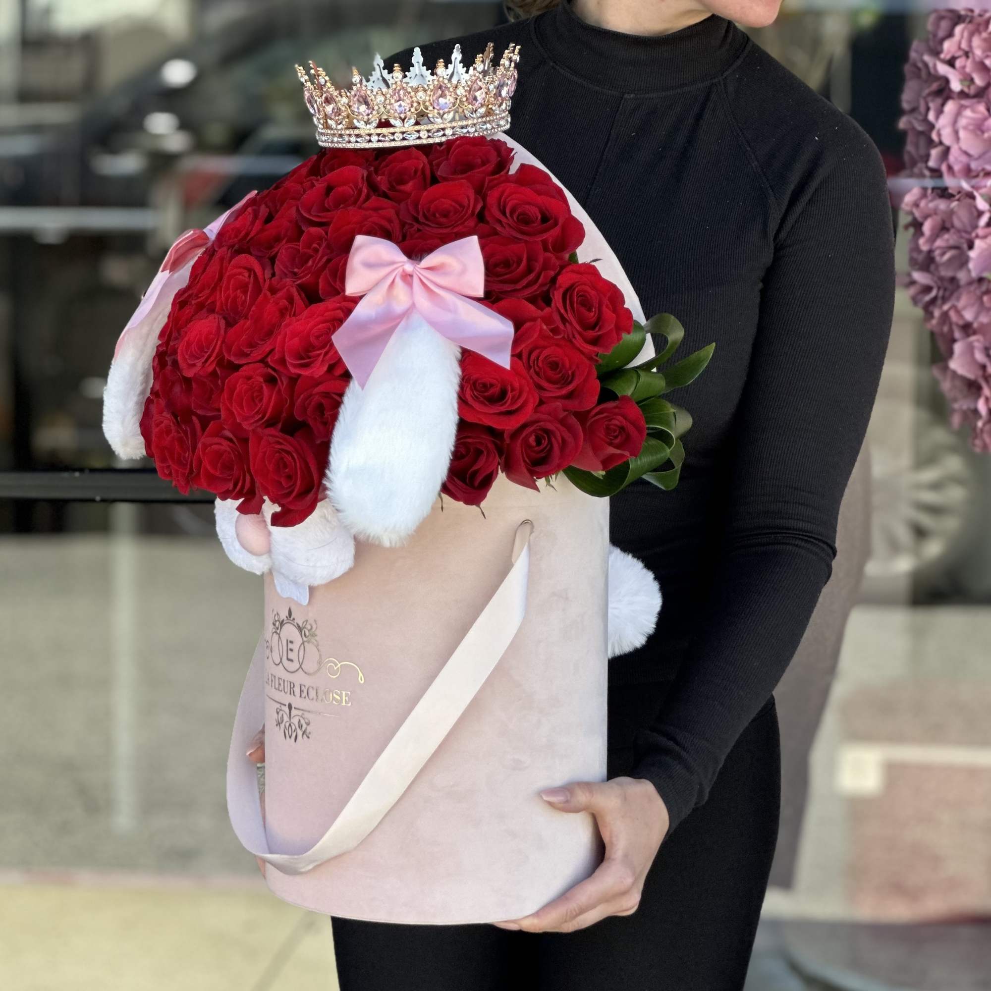 Large bouquet of red roses with a crown and pink bow in a round box