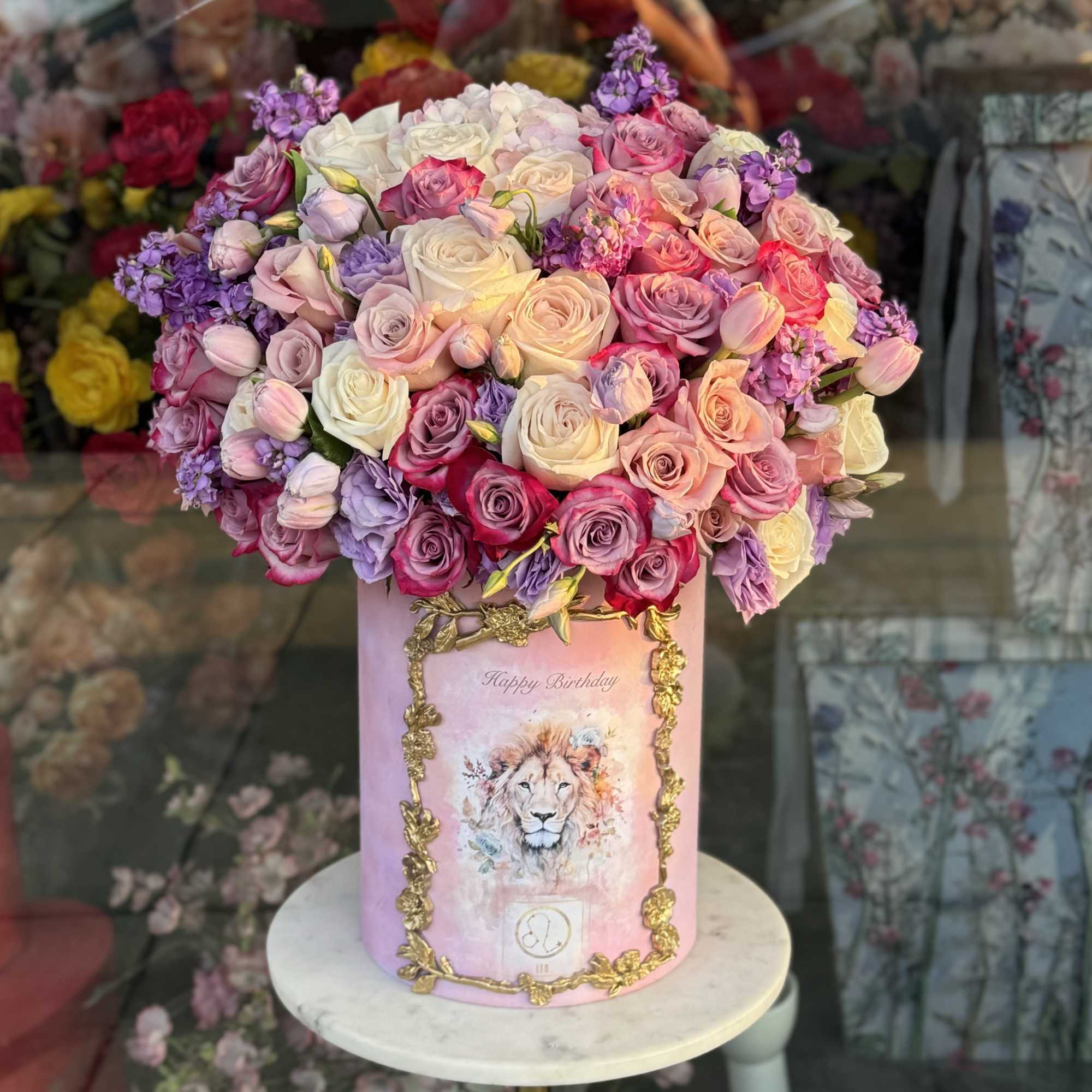 Pink and lavender roses arranged in a tall pink box with a lion illustration