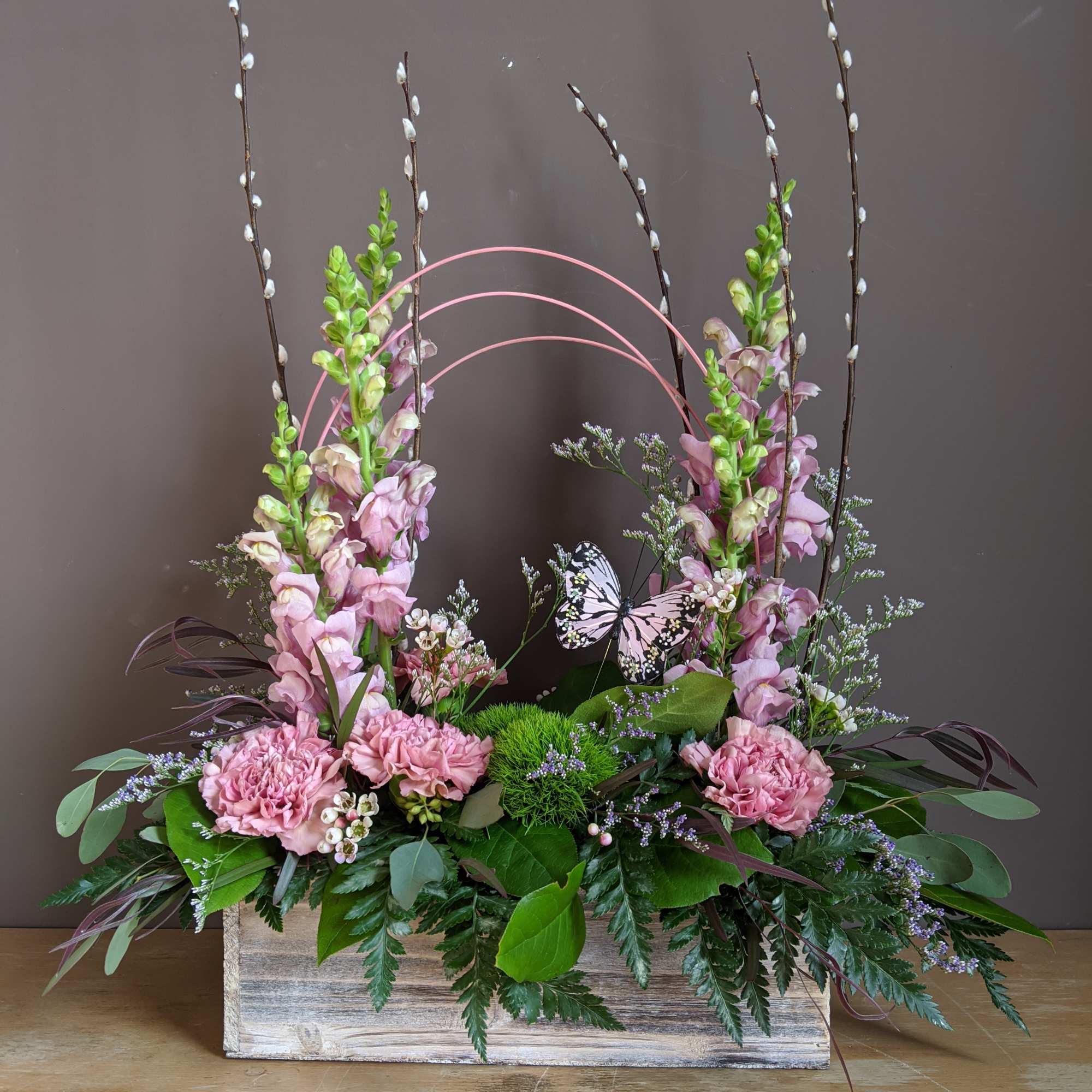 Pink floral arrangement in a wooden box with tall branches and a butterfly accent
