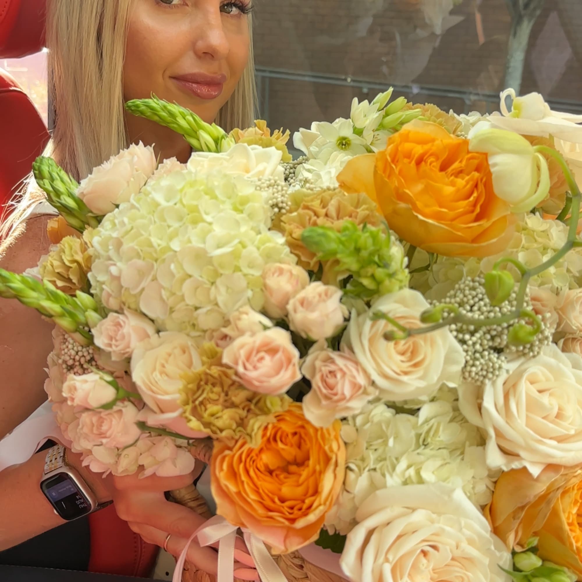 Woman holding a large bouquet of cream, peach, and orange flowers in a woven basket