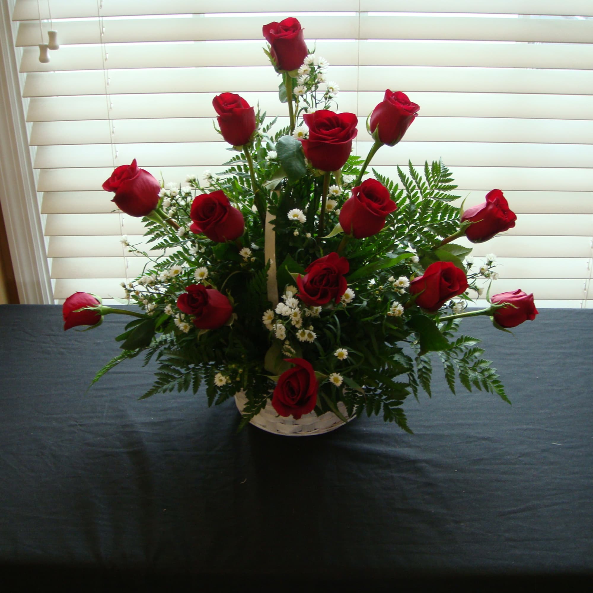 Red roses arranged in a white basket with greenery and small white filler flowers