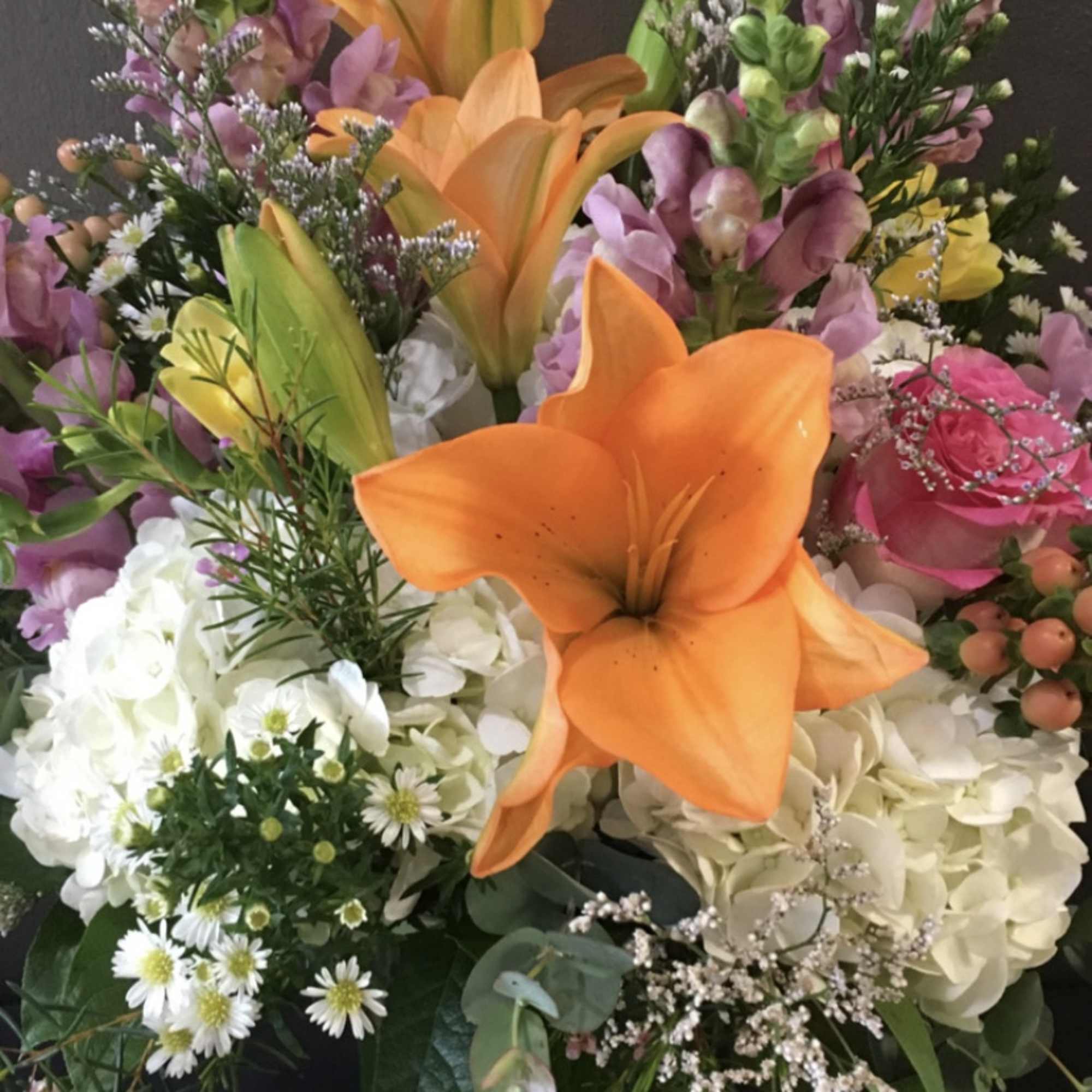 Mixed arrangement with orange lilies, white hydrangeas, pink roses, and other blooms in a clear glass vase.