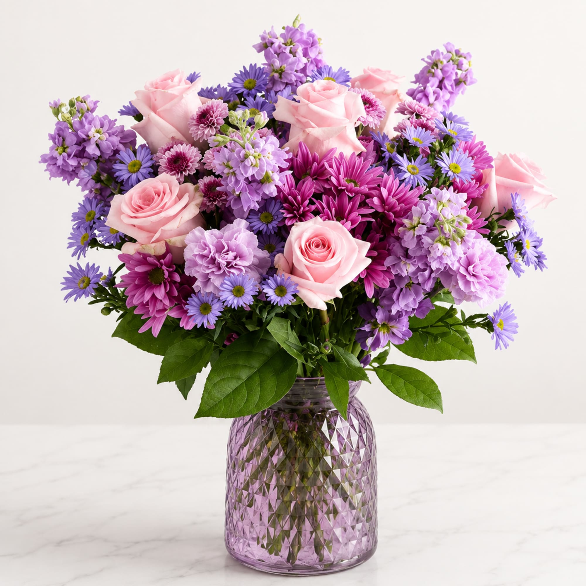 A charming garden-style bouquet featuring soft pink roses, lavender stock, purple daisies