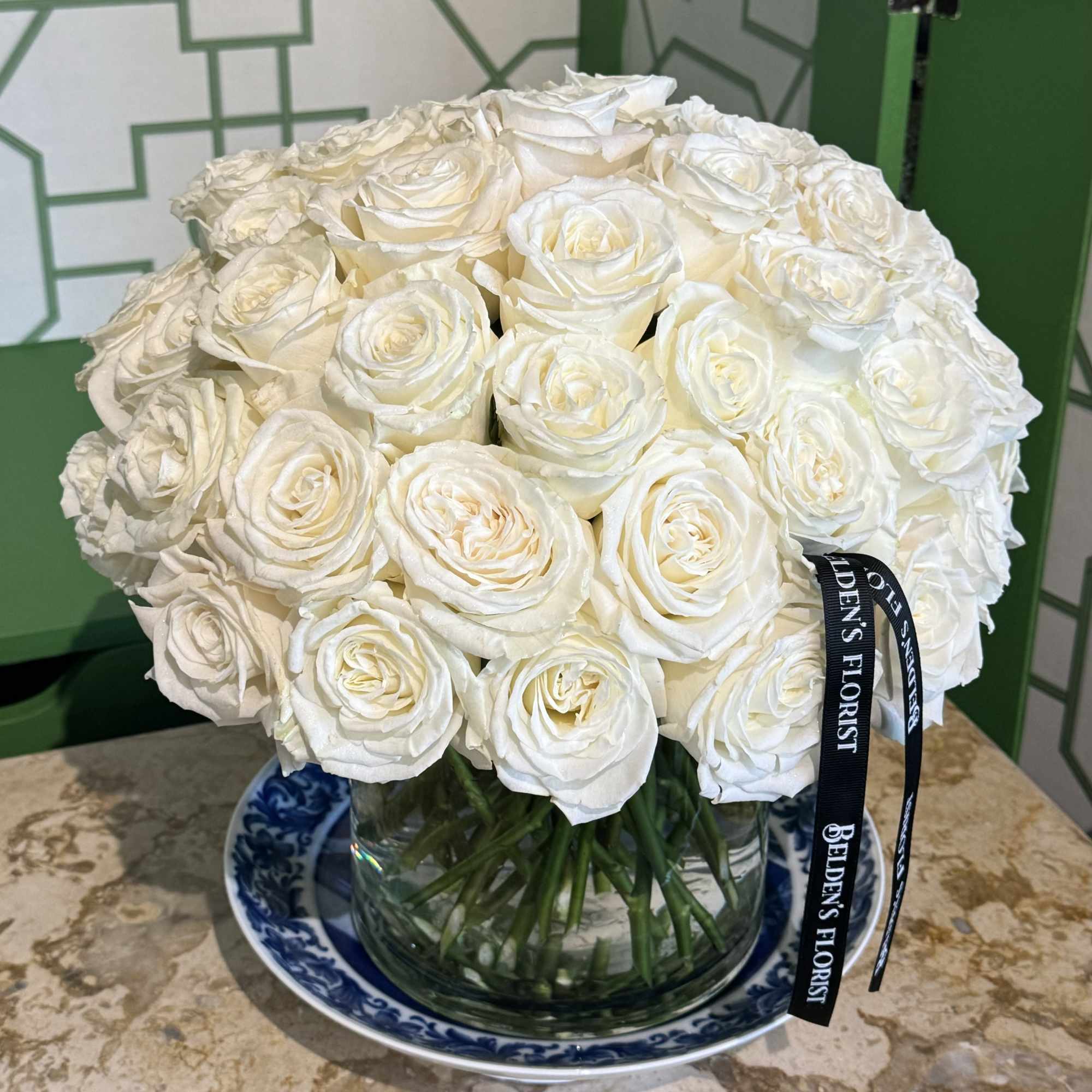 A round bouquet of white roses in a glass vase on a blue-and-white plate.