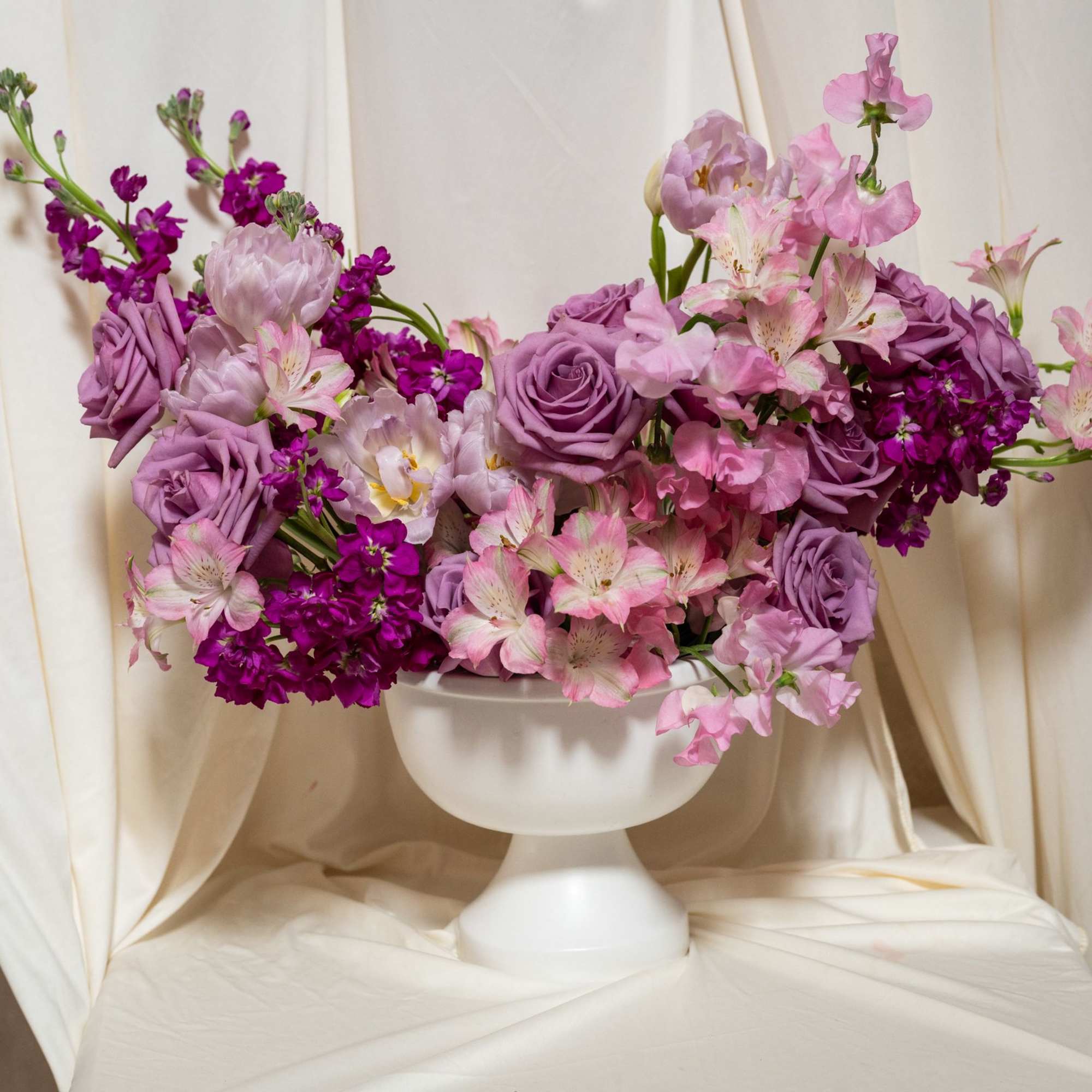Pink and purple floral arrangement in a white pedestal vase